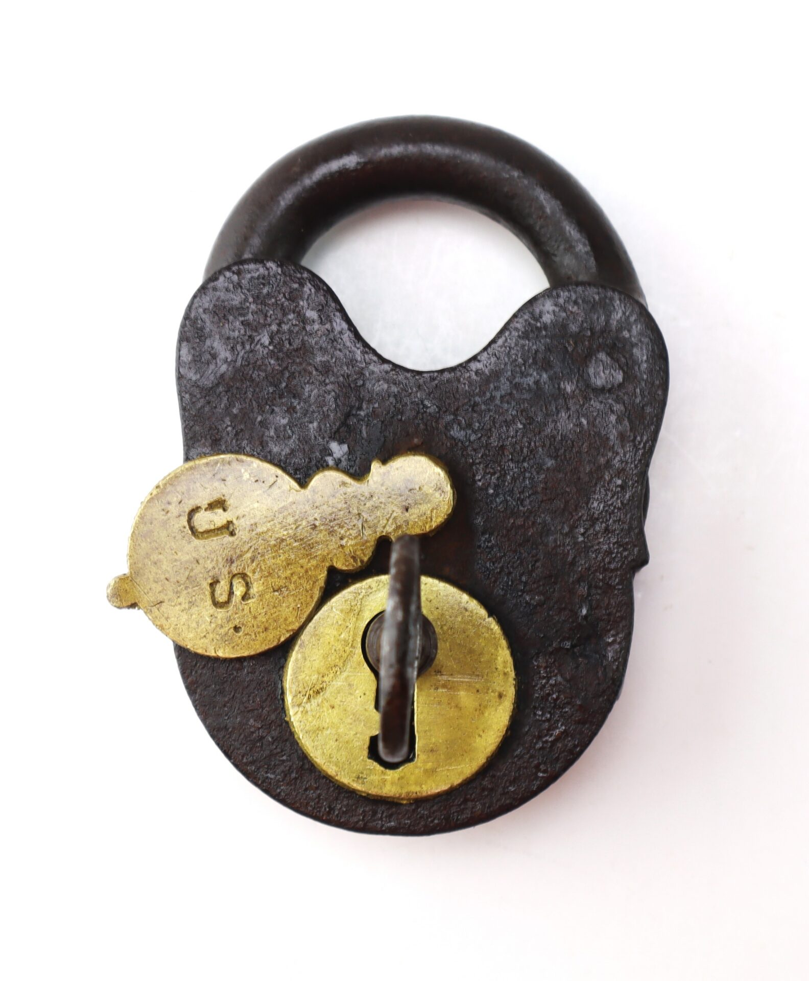 Antique iron padlock with a brass key marked “U.S.” inserted into the keyhole, photographed on a white background.