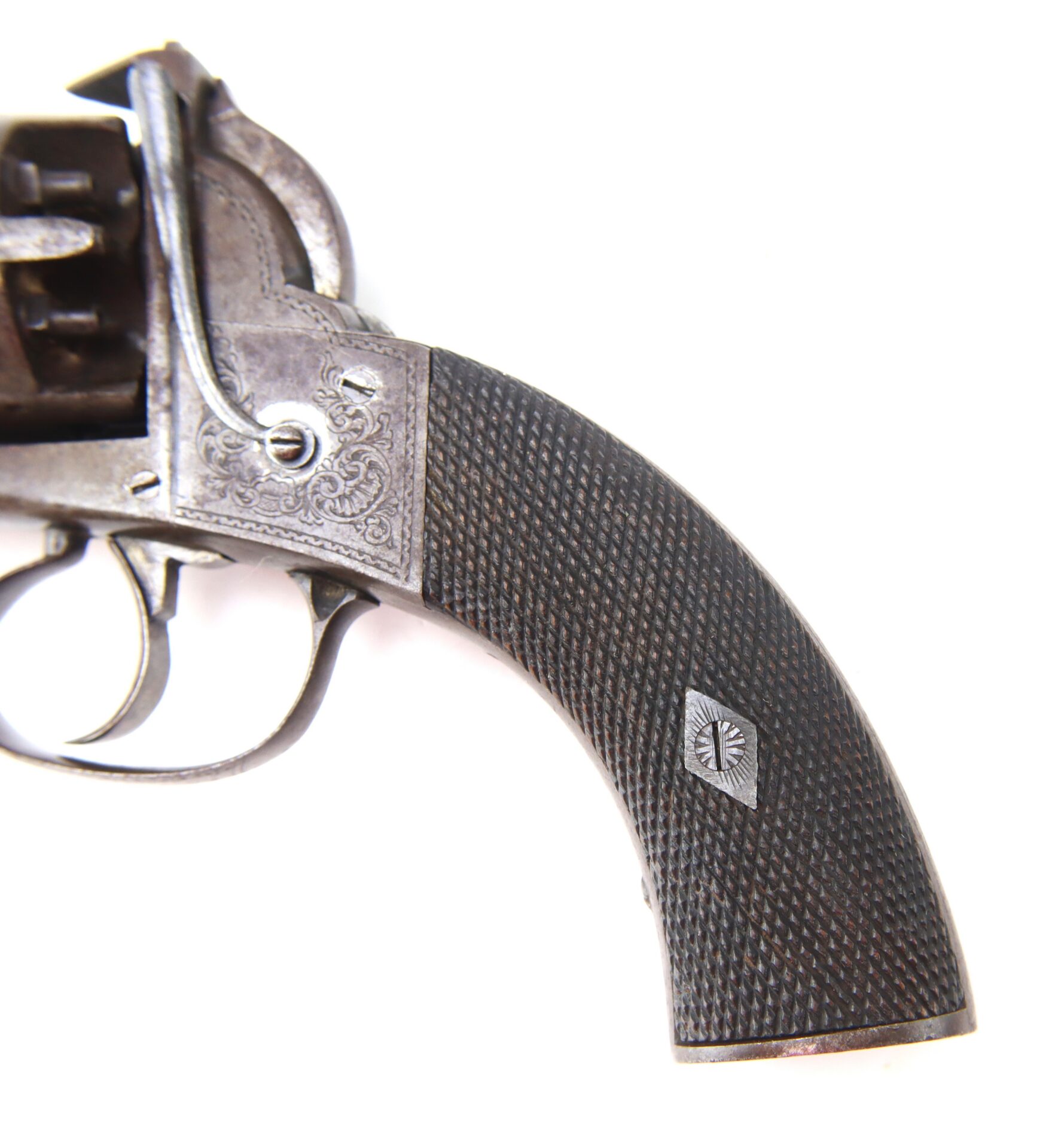 Close-up of the textured wooden grip and trigger area of an antique revolver with engraved metal detailing, all set against a white background.