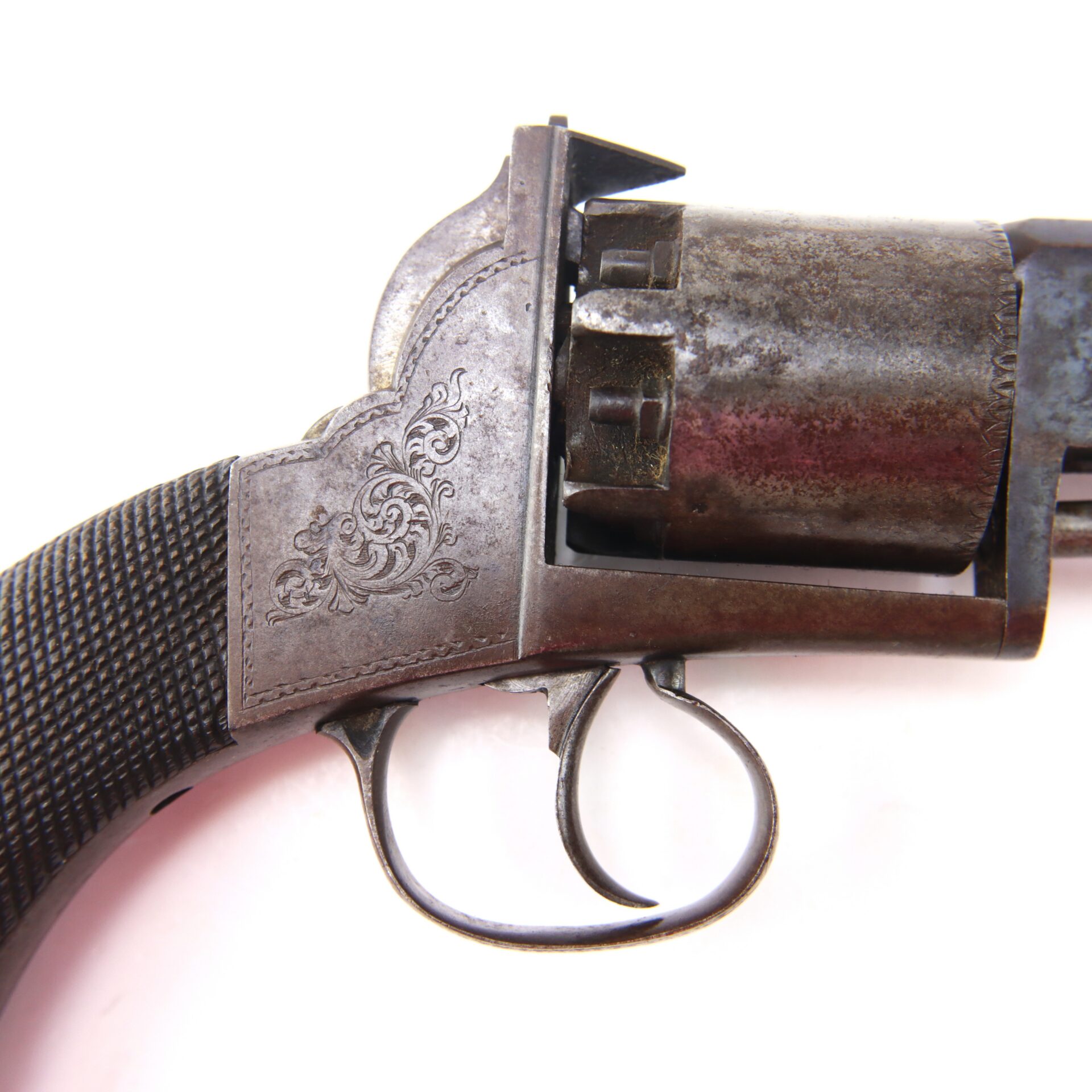 Close-up of a vintage revolver’s trigger and engraved handle against a white background.