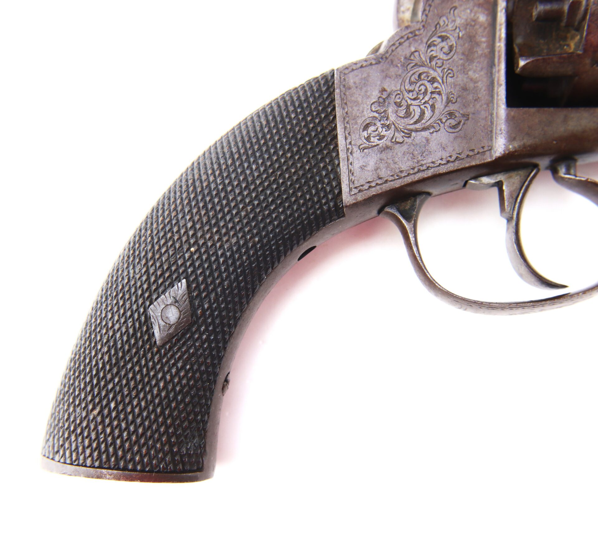 Close-up of an antique revolver’s grip and trigger, showing engraved metalwork and textured handle design against a white background.