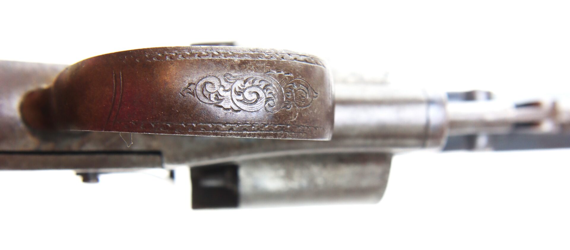 Close-up of an engraved metal trigger guard on a vintage firearm against a white background.