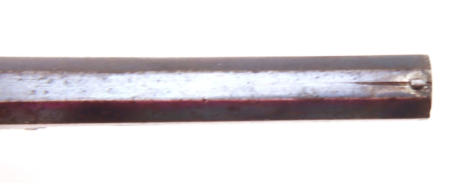 Close-up of a metal rod with a scratch and a small indentation near the edge, set against a white background.