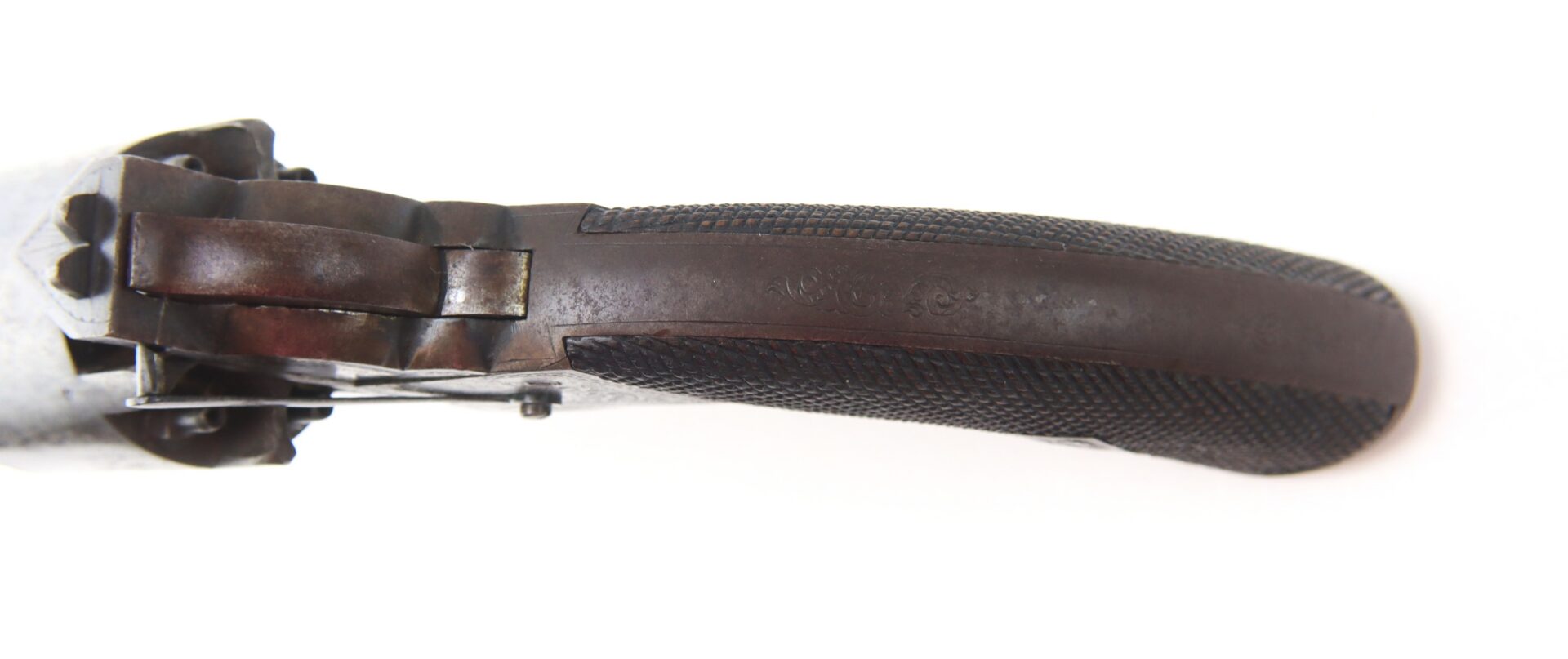 Close-up view of the checkered dark wooden grip and trigger guard of a vintage firearm, photographed from above on a white background.