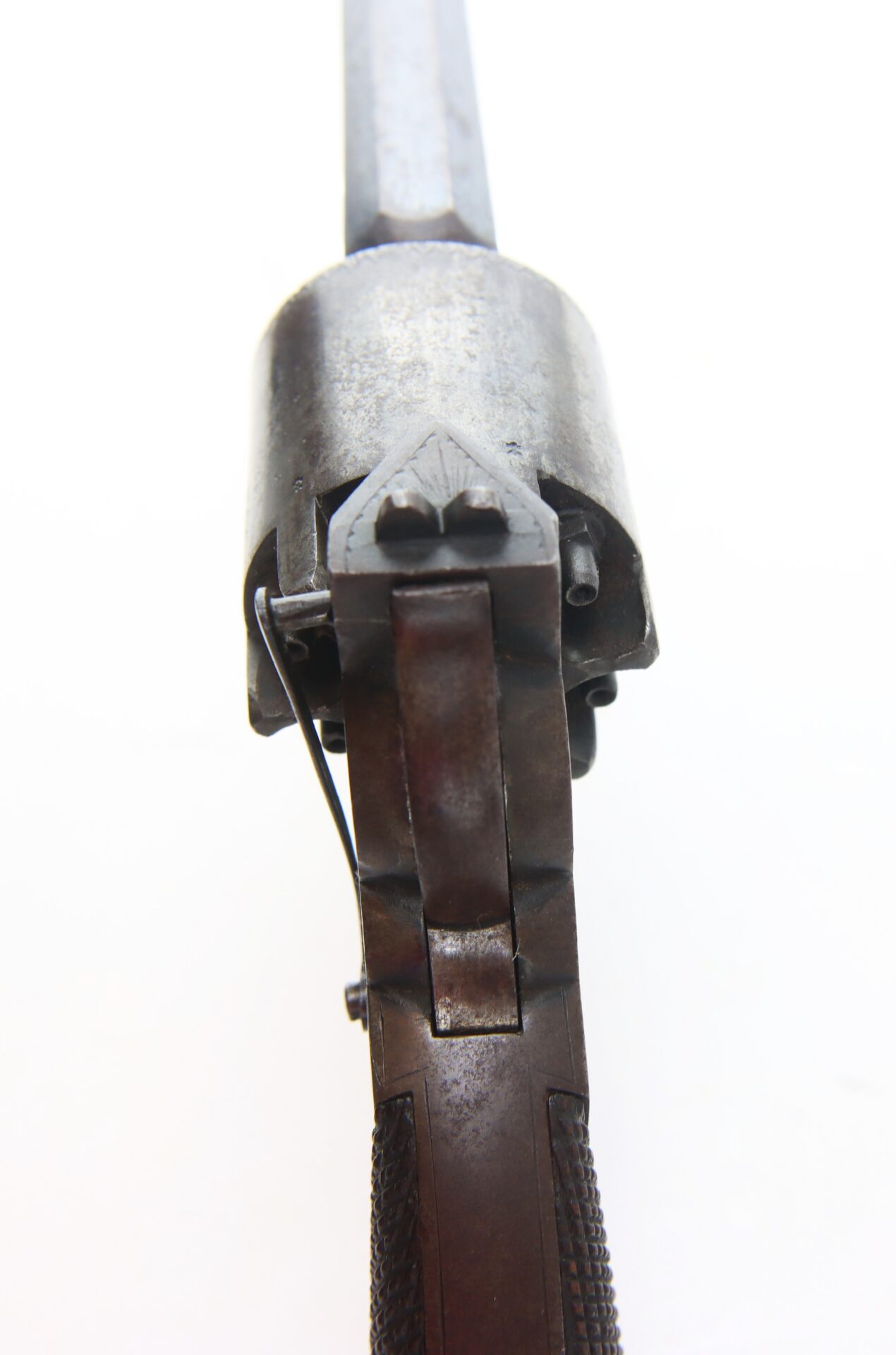 Close-up view of the back and cylinder of an antique revolver, showing metal details and part of the handle against a white background.