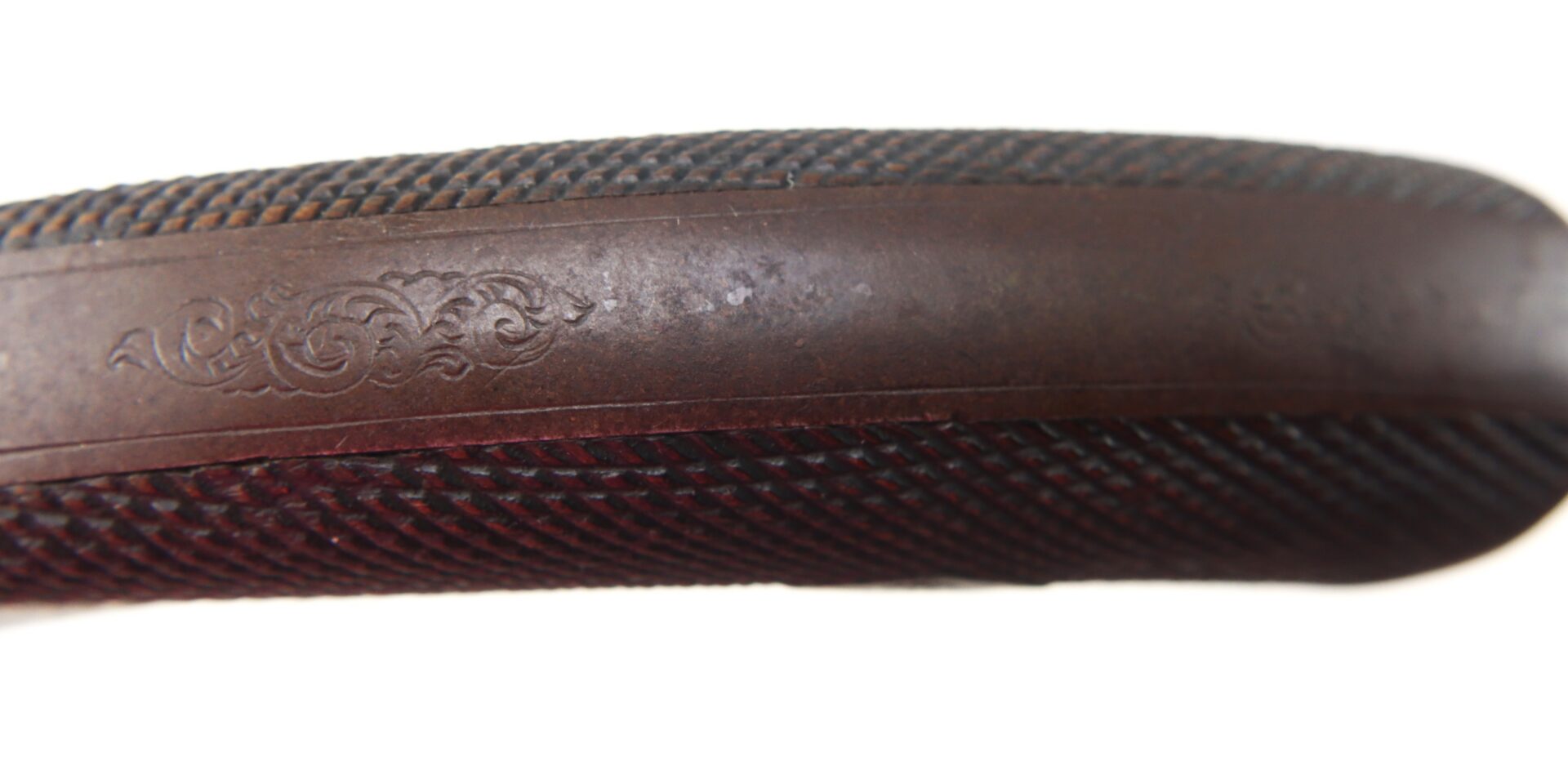 Close-up of a brown, textured object with a subtle, decorative engraved pattern on a smooth band along its surface.