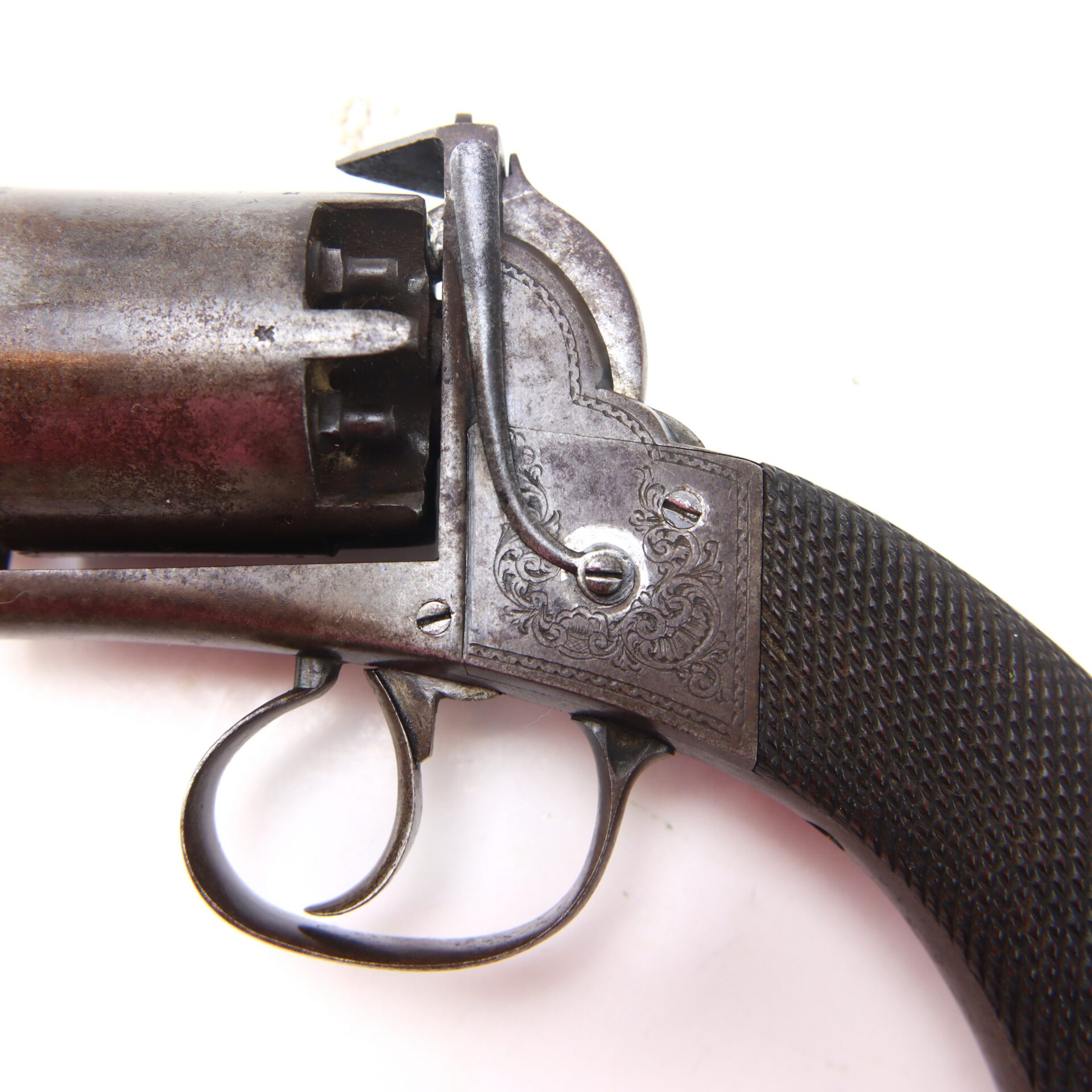 Close-up of the trigger, grip, and part of the cylinder of an antique revolver with engraved metal and a textured handle.