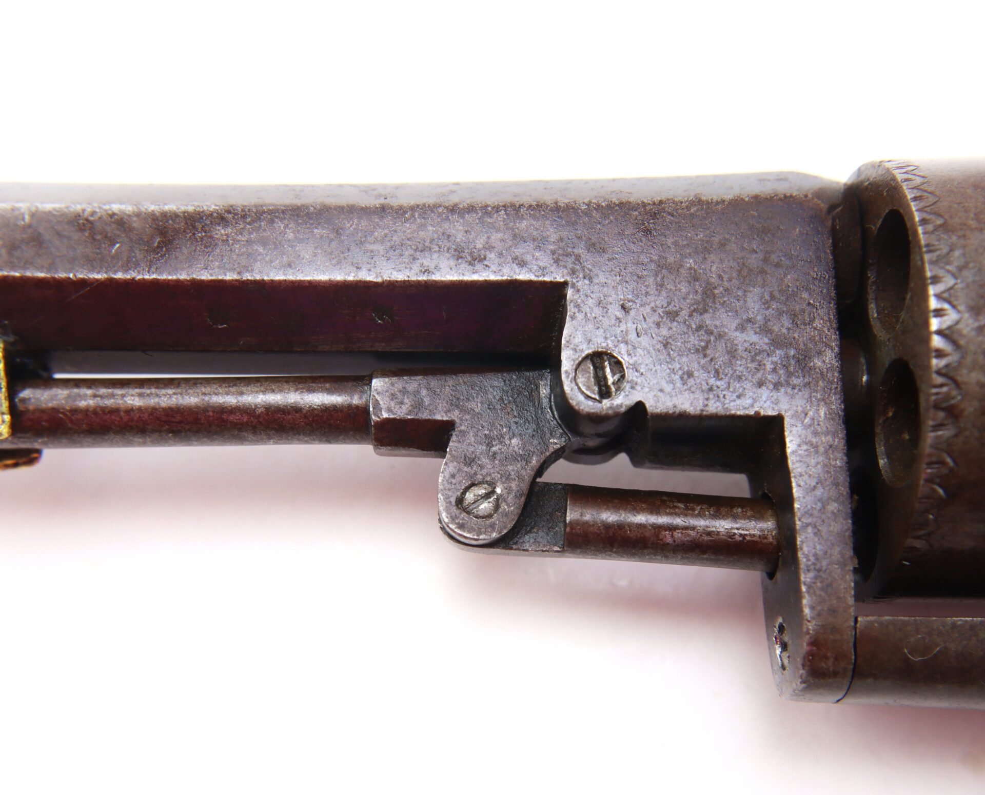 Close-up view of an old, metal revolver showing part of the cylinder, frame, and screws against a white background.