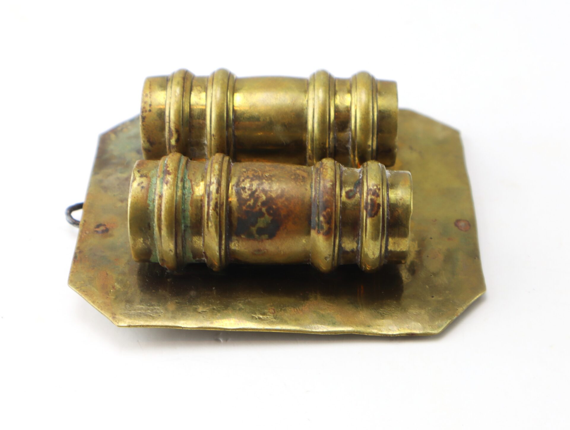 A brass military insignia featuring two crossed cannons mounted on a flat, rectangular brass plate with slightly beveled corners.