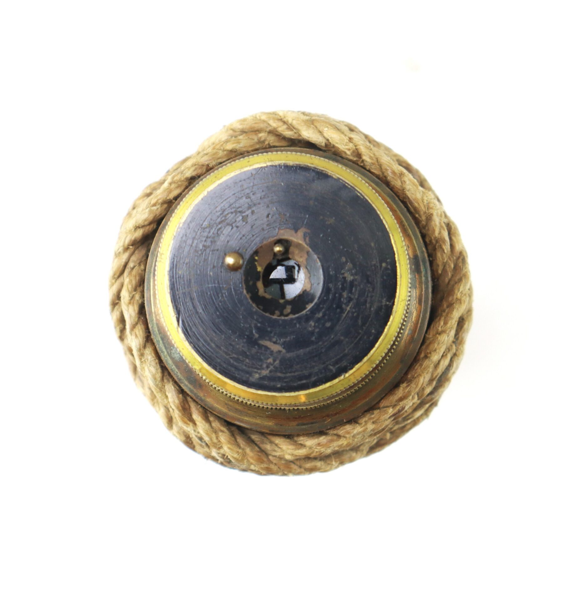 A round vintage brass nautical compass with a glass face is coiled with thick rope around its edge, viewed from above on a white background.