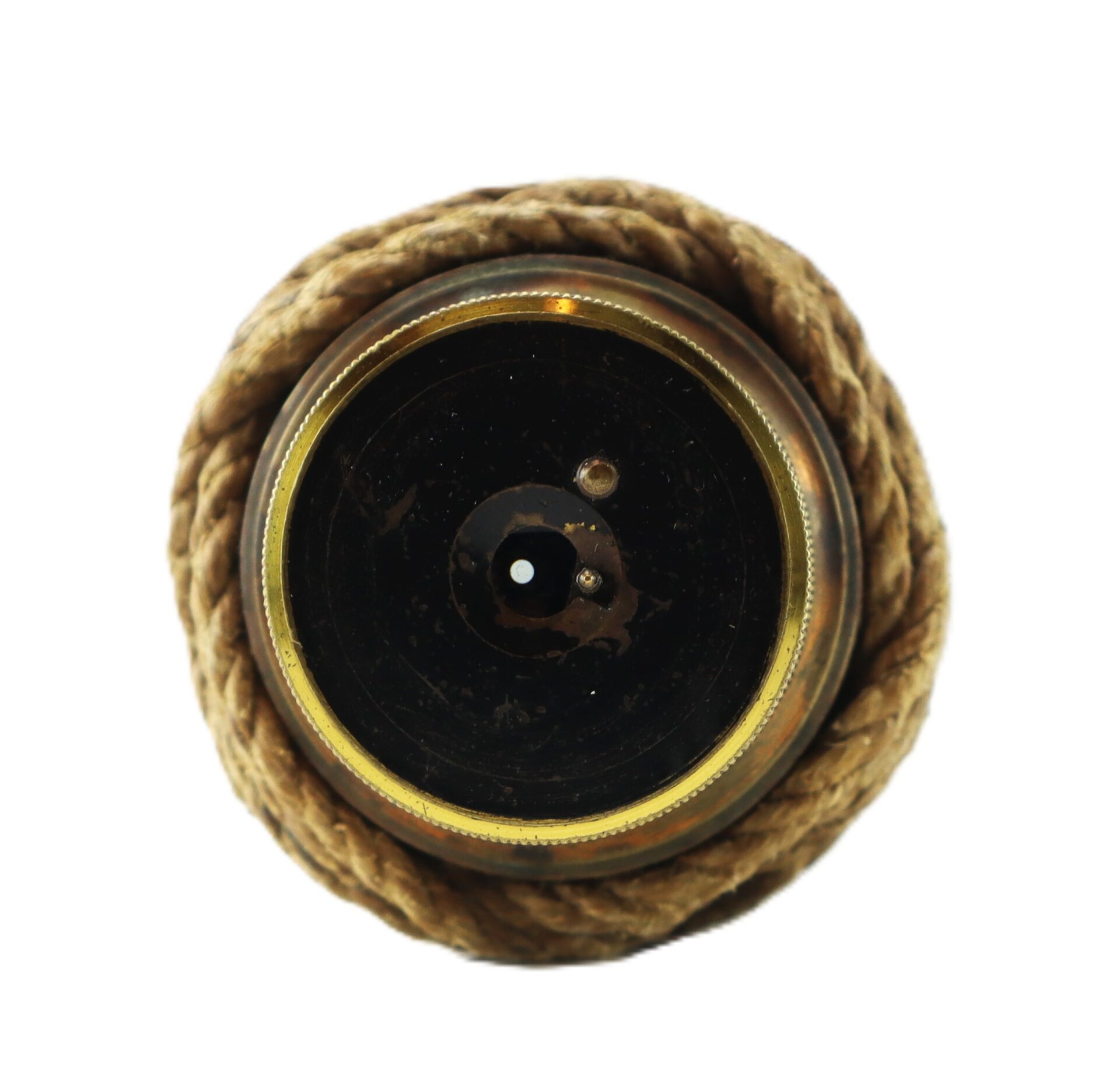 Close-up of a round, brass object with a black center and rope wrapped around its edge, viewed from above against a white background.