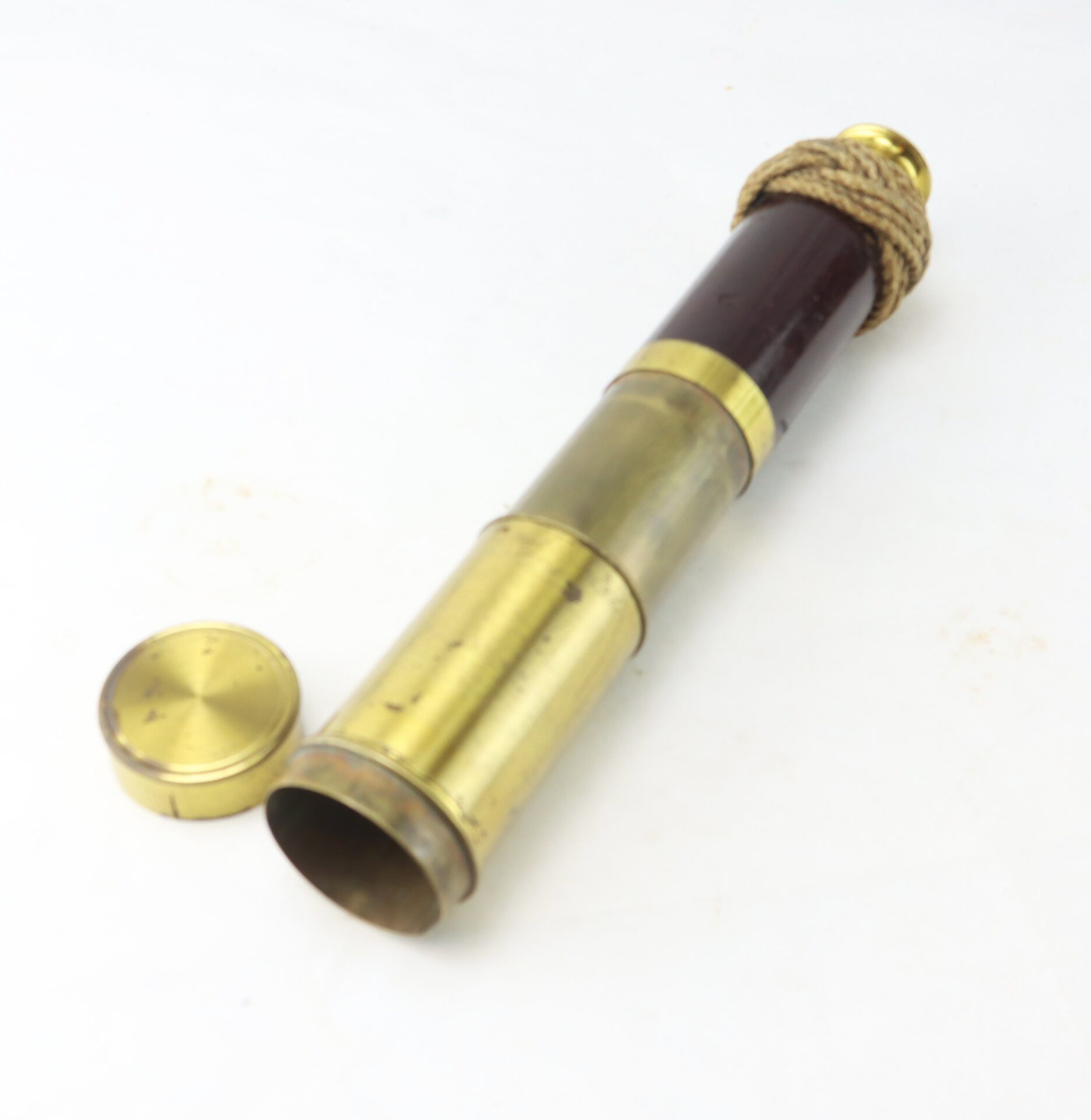 A brass and wood handheld telescope with a rope grip, extended, and its cap placed beside it on a white background.