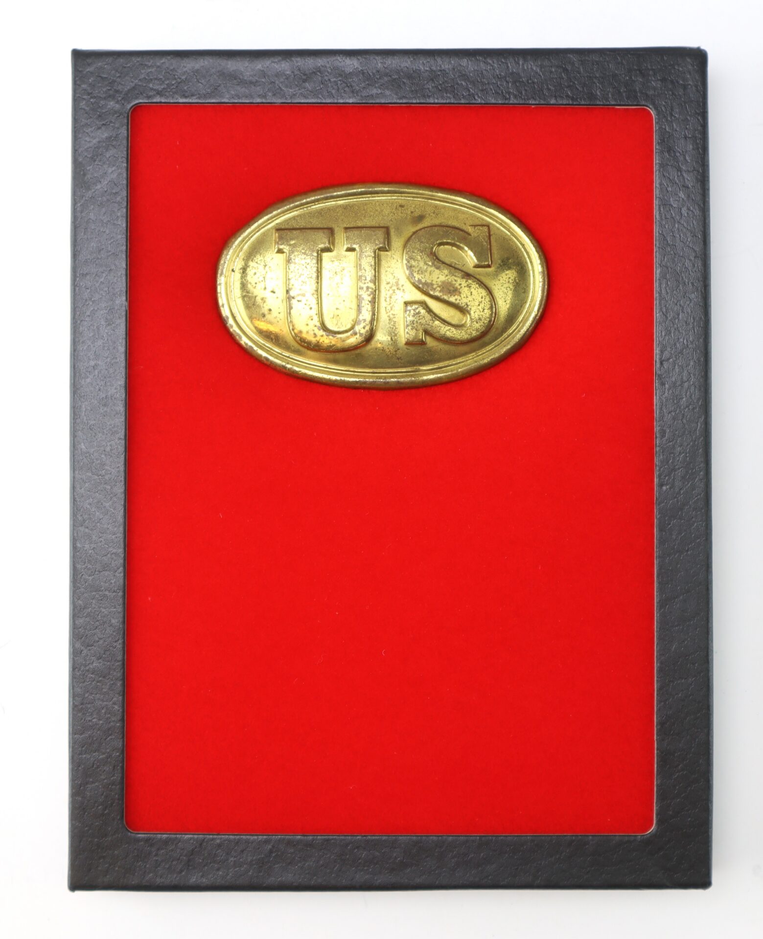 A brass oval plaque with “US” embossed, mounted on red felt inside a black frame.