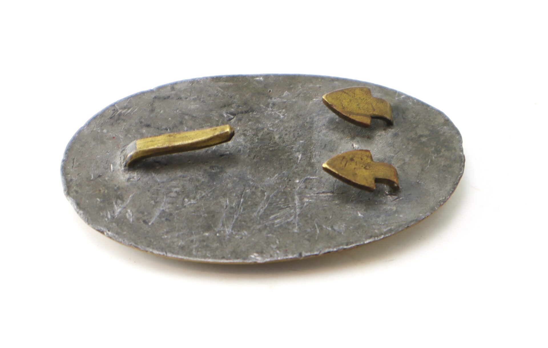 Oval metal badge back with two bent prong fasteners and a single bar, showing wear and minor scratches.