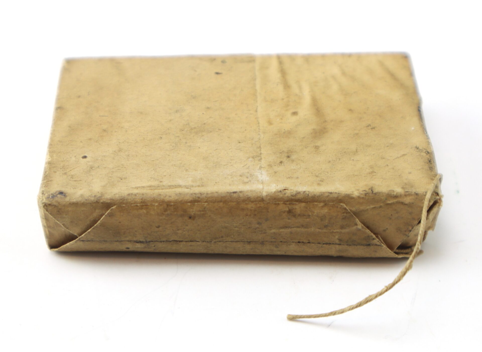 A small rectangular package wrapped in brown paper, with neatly folded corners and a short length of string attached.