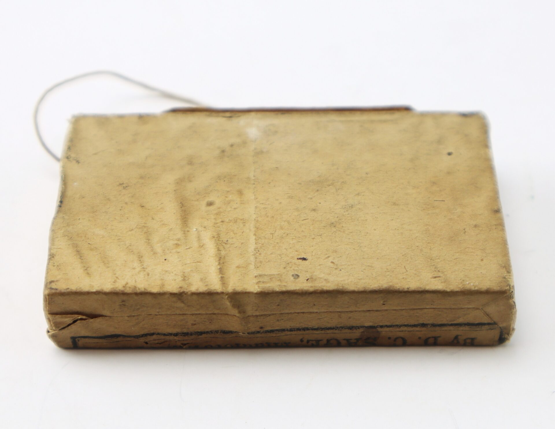 Small, rectangular, brown paper-wrapped package with visible creases and a thin string attached, placed on a white background.