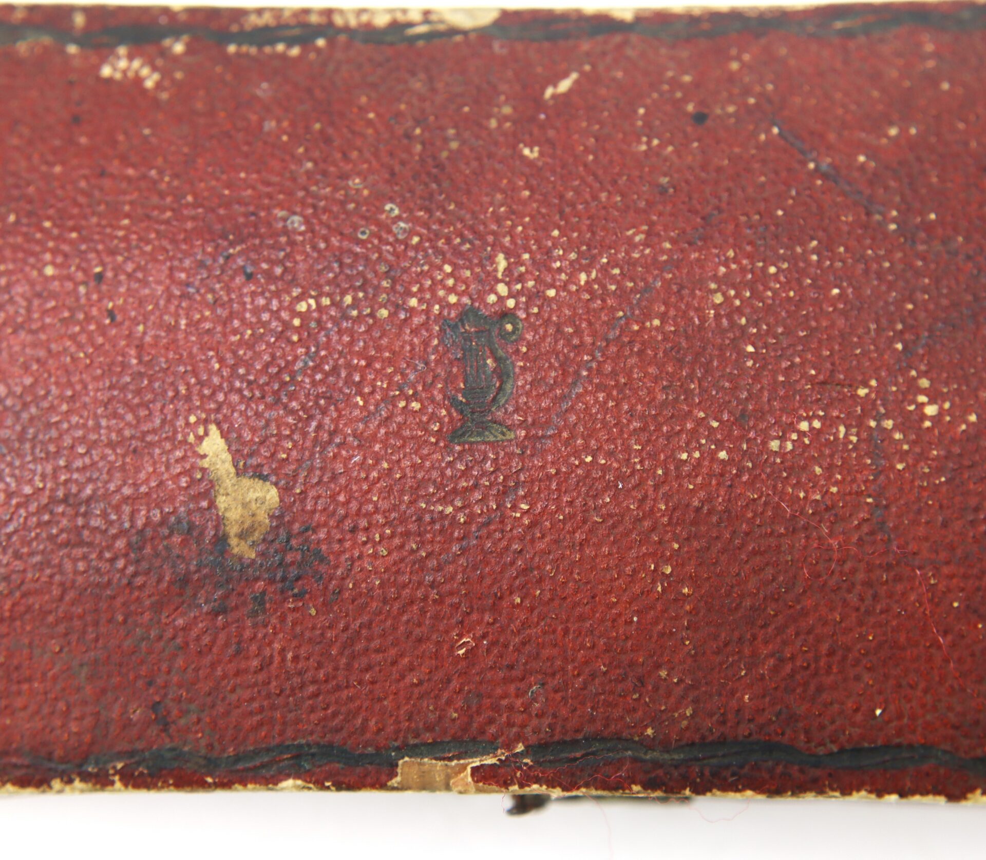 Close-up of worn red textured leather on the AUTO-DRAFT (Copy) product, featuring a small, faded black symbol resembling a stylized letter “J” or “T” in the center.