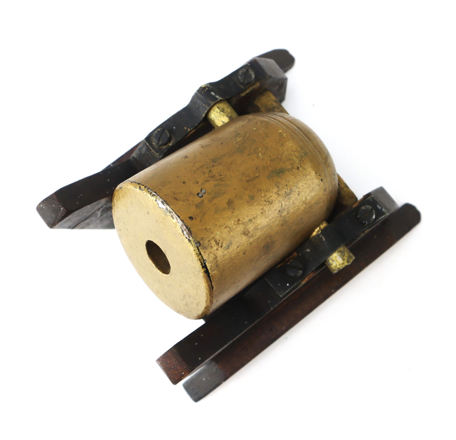 Brass cylindrical object with a hole in the center, mounted on a wooden and metal base, against a white background.