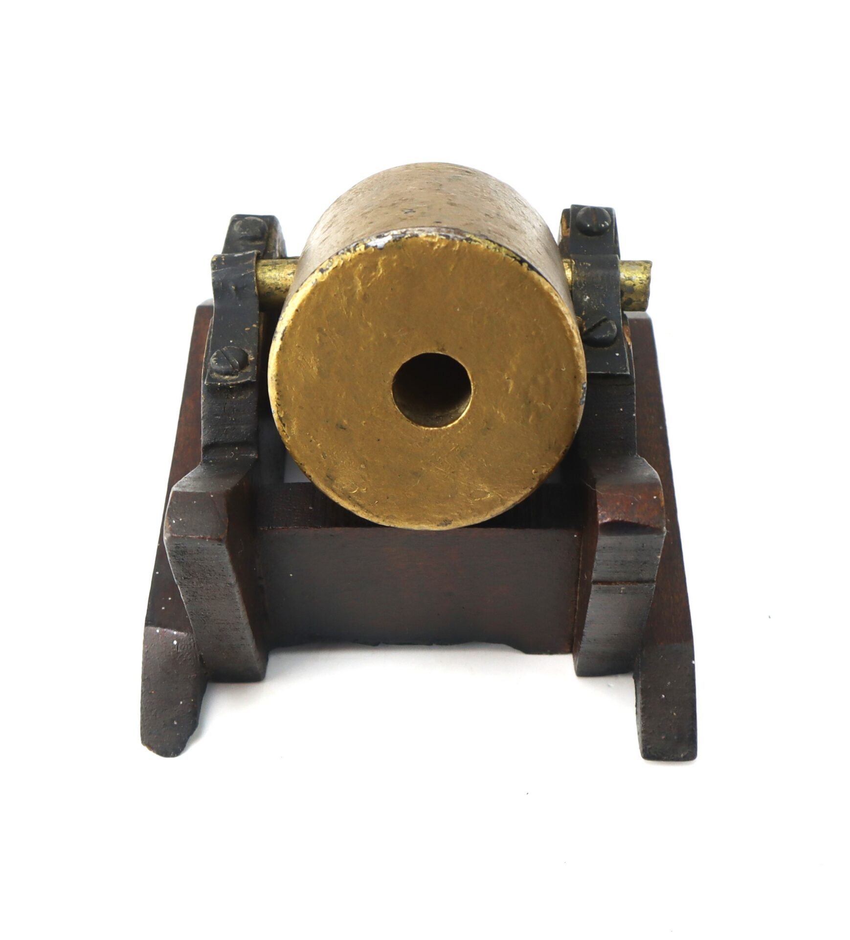 A small brass cannon model on a wooden base, viewed from the muzzle end, showing the circular barrel opening and mounting brackets.