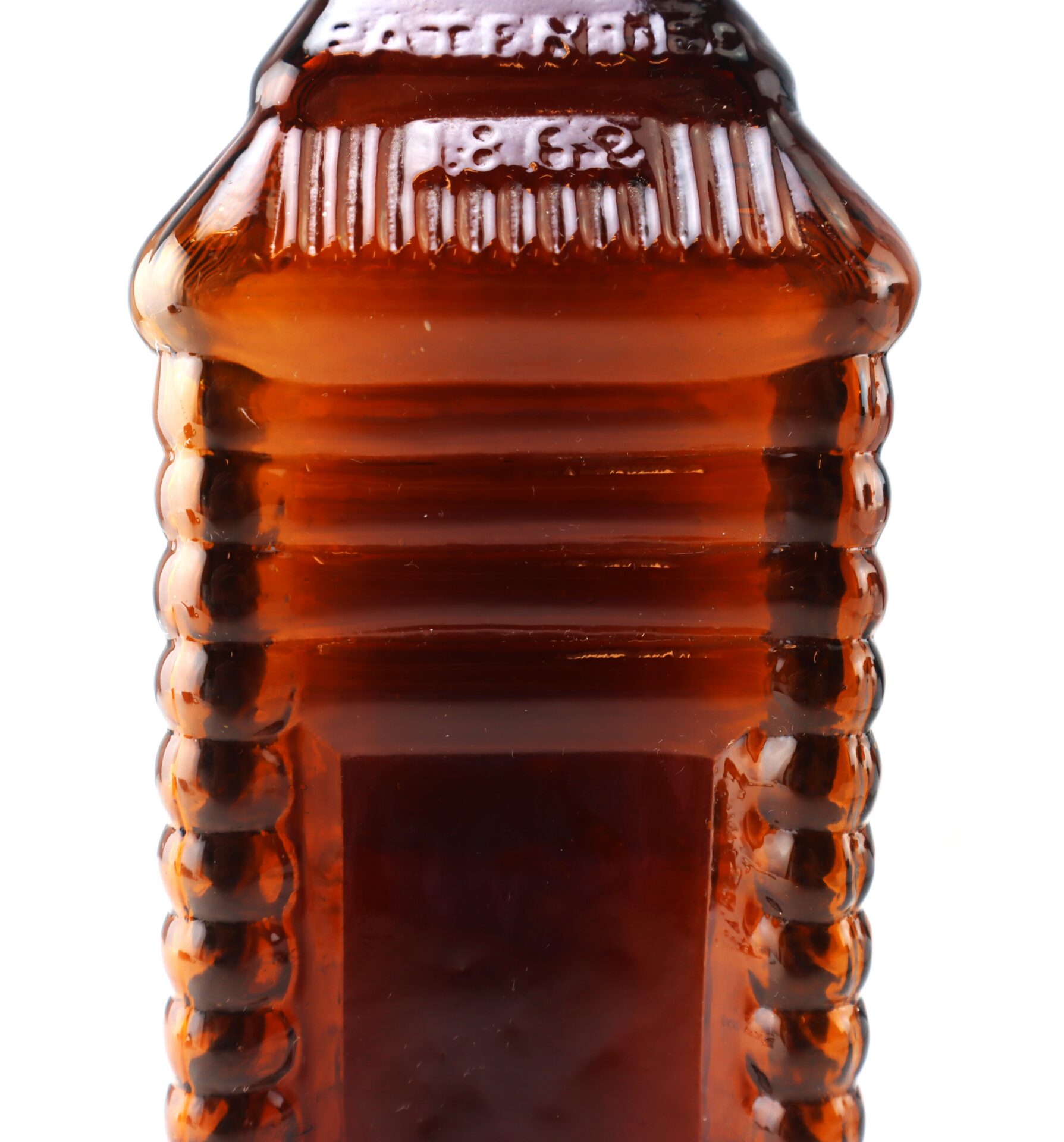 Close-up of a vintage ribbed amber glass bottle with rectangular panels, embossed markings, and a white background.