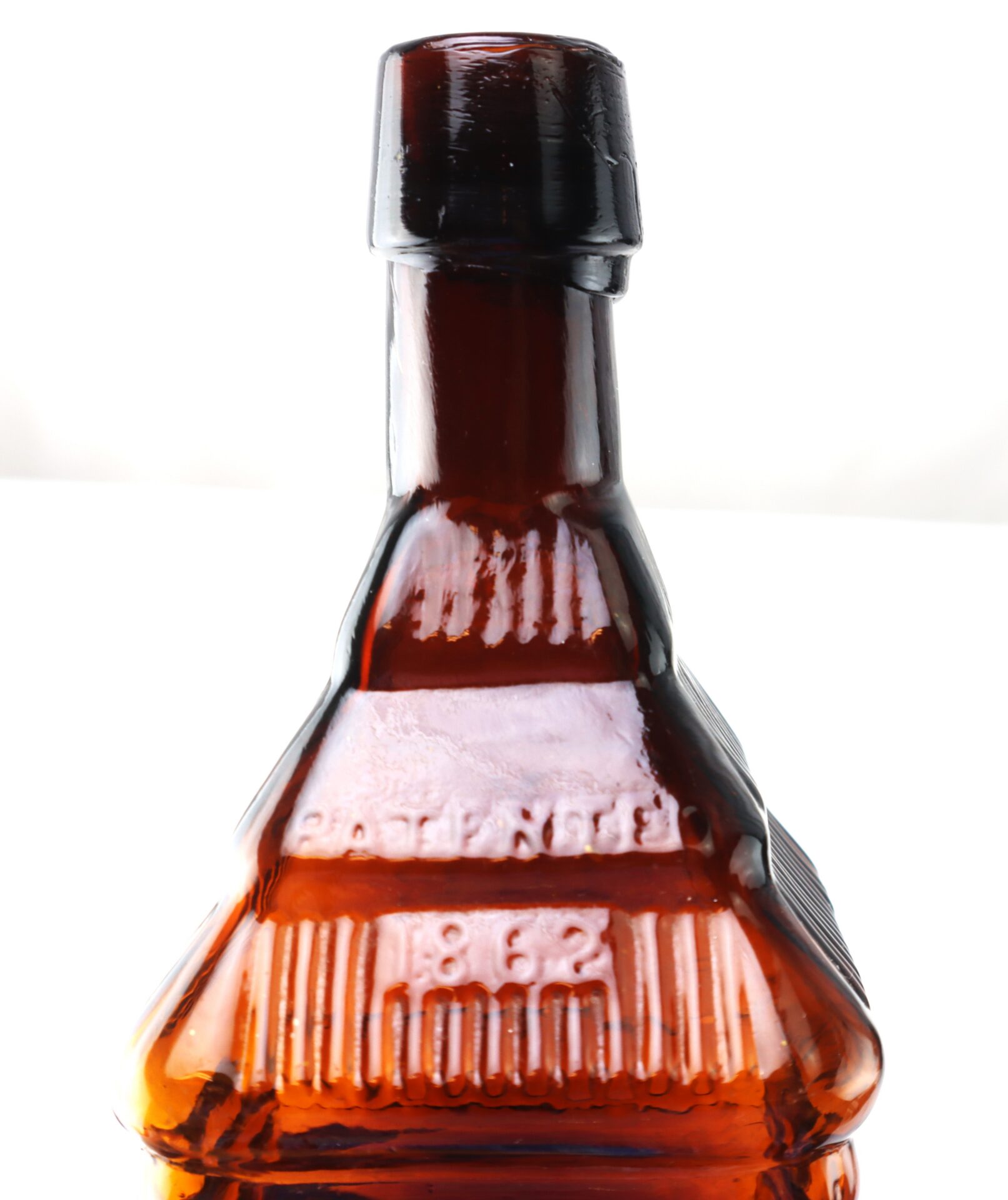 Close-up of an amber glass bottle with embossed text and the number “862” on its neck, against a white background.