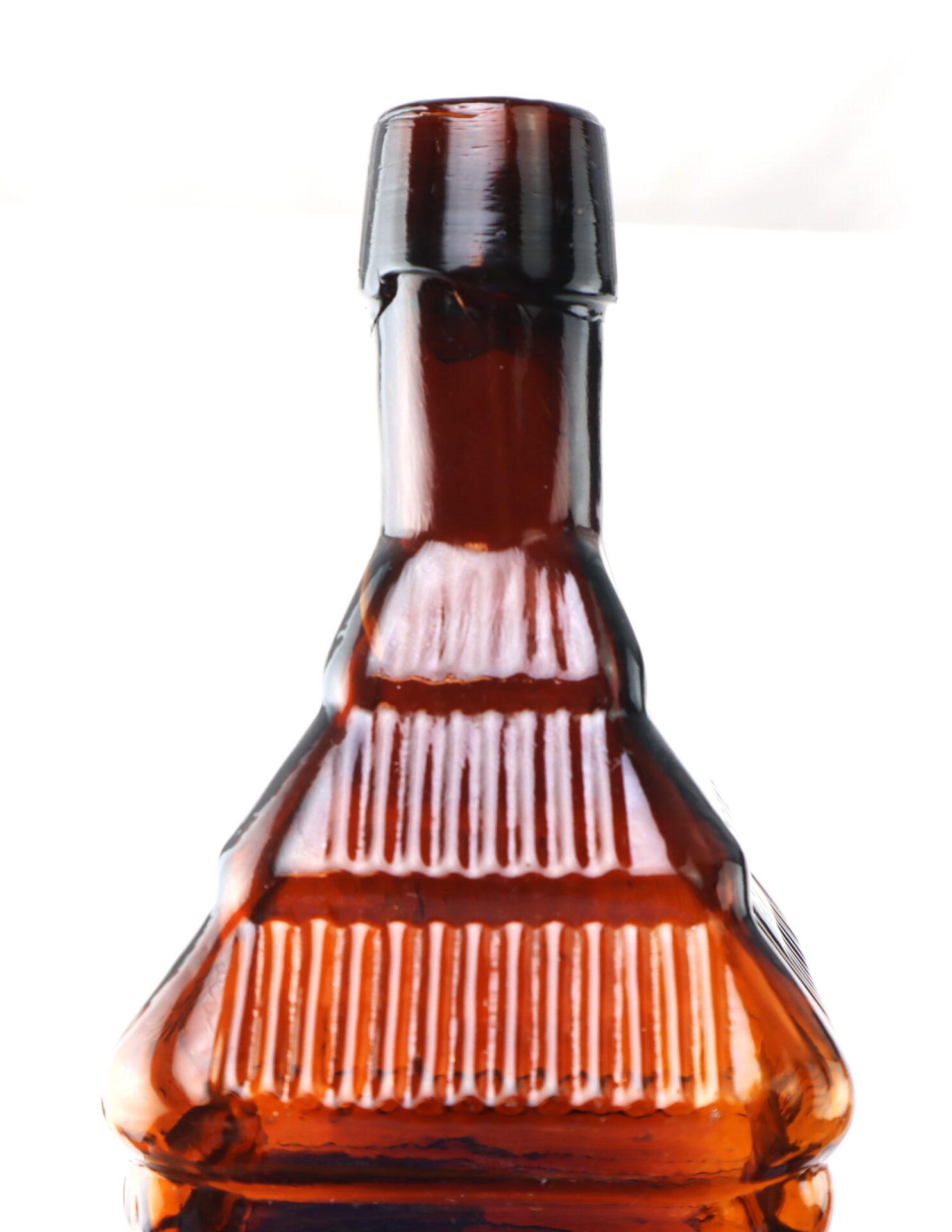 A close-up of the top half of a ribbed, amber-colored glass bottle against a white background.