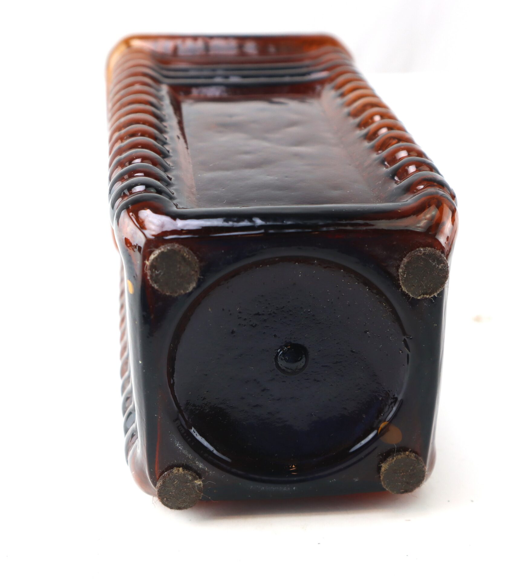 A brown glass bottle is shown lying on its side, revealing a circular base with four small felt pads at the corners.