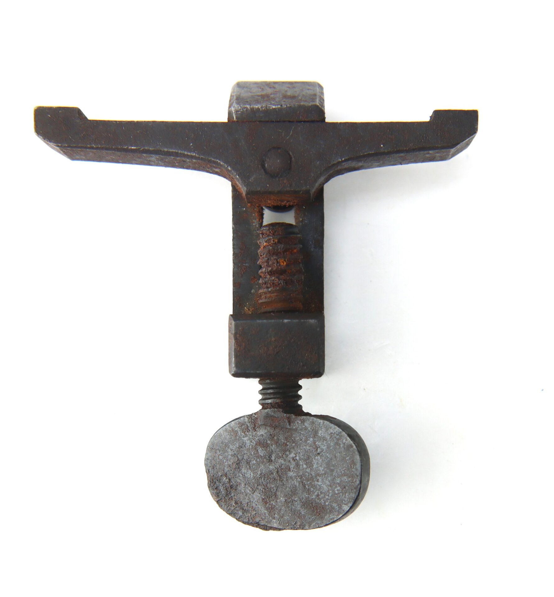 Old rusty metal clamp with a T-shaped top, central screw mechanism, and a rounded bottom plate, positioned vertically on a plain white background.