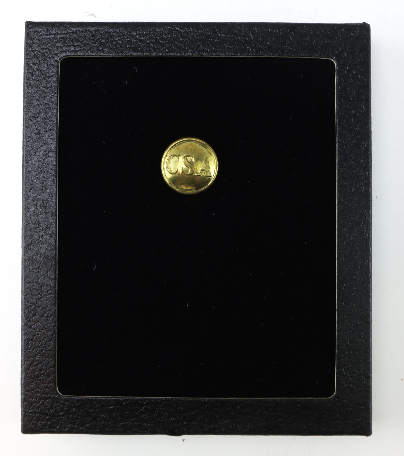 A small gold button engraved with “CSA” is displayed in the center of a black velvet-lined, square black case.