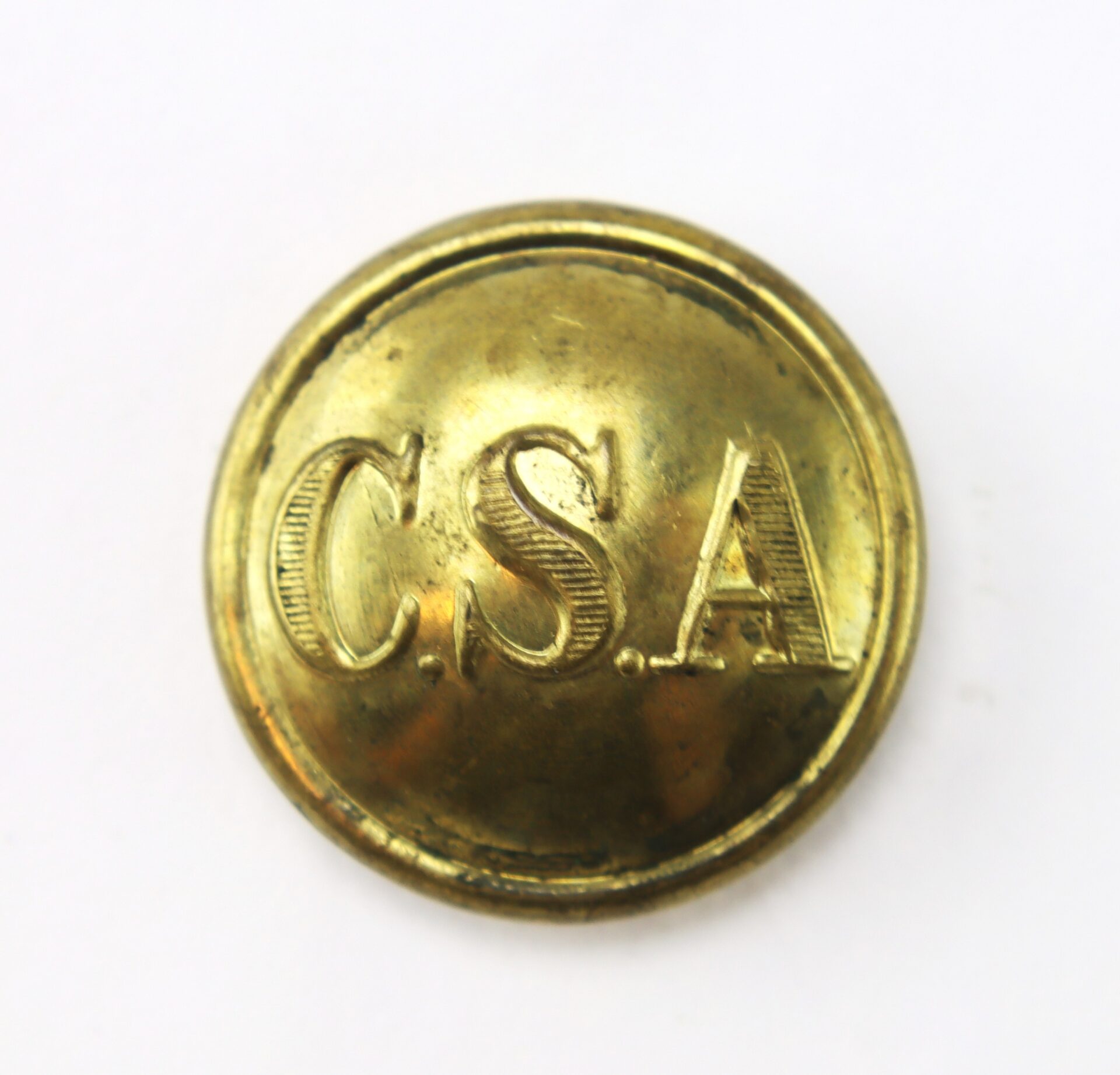 A round brass button with the letters “C.S.A.” engraved on its surface, photographed against a white background.