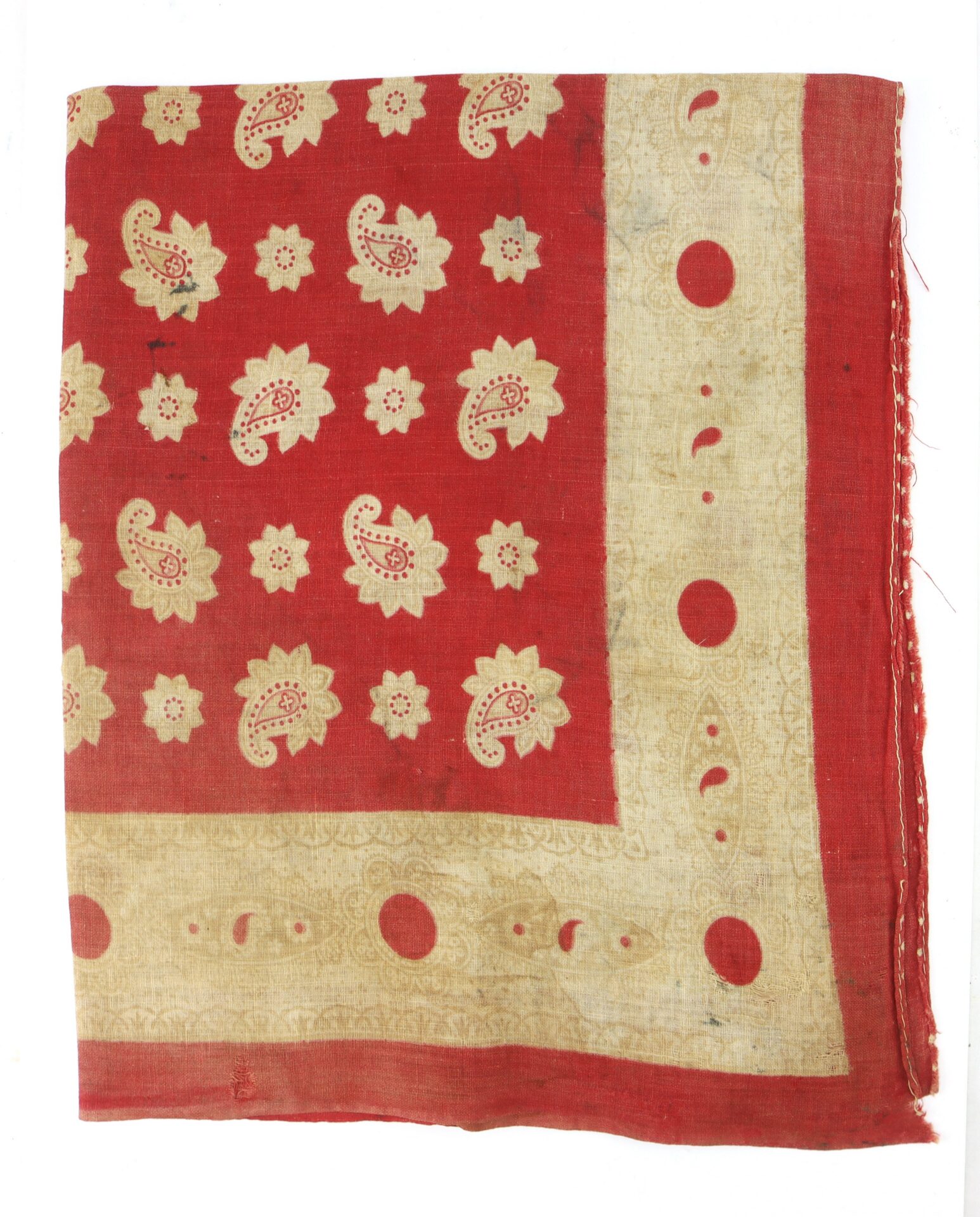 Square red cloth with cream border, featuring a pattern of cream paisley and floral motifs in the center and circles along the border.