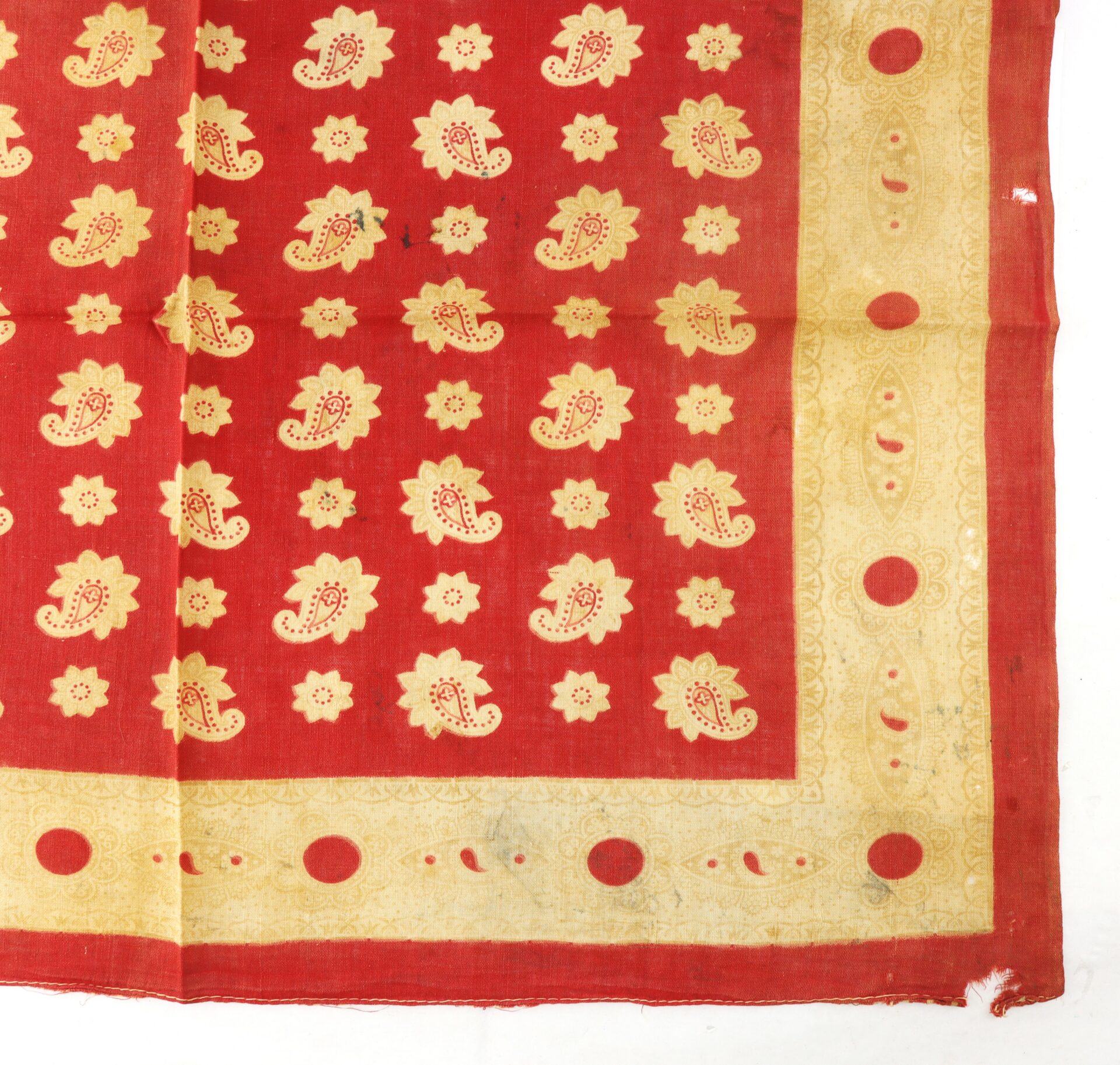 Red cloth with a yellow border, decorated with repeating floral and paisley patterns in yellow, arranged in rows, with visible creases on the fabric.