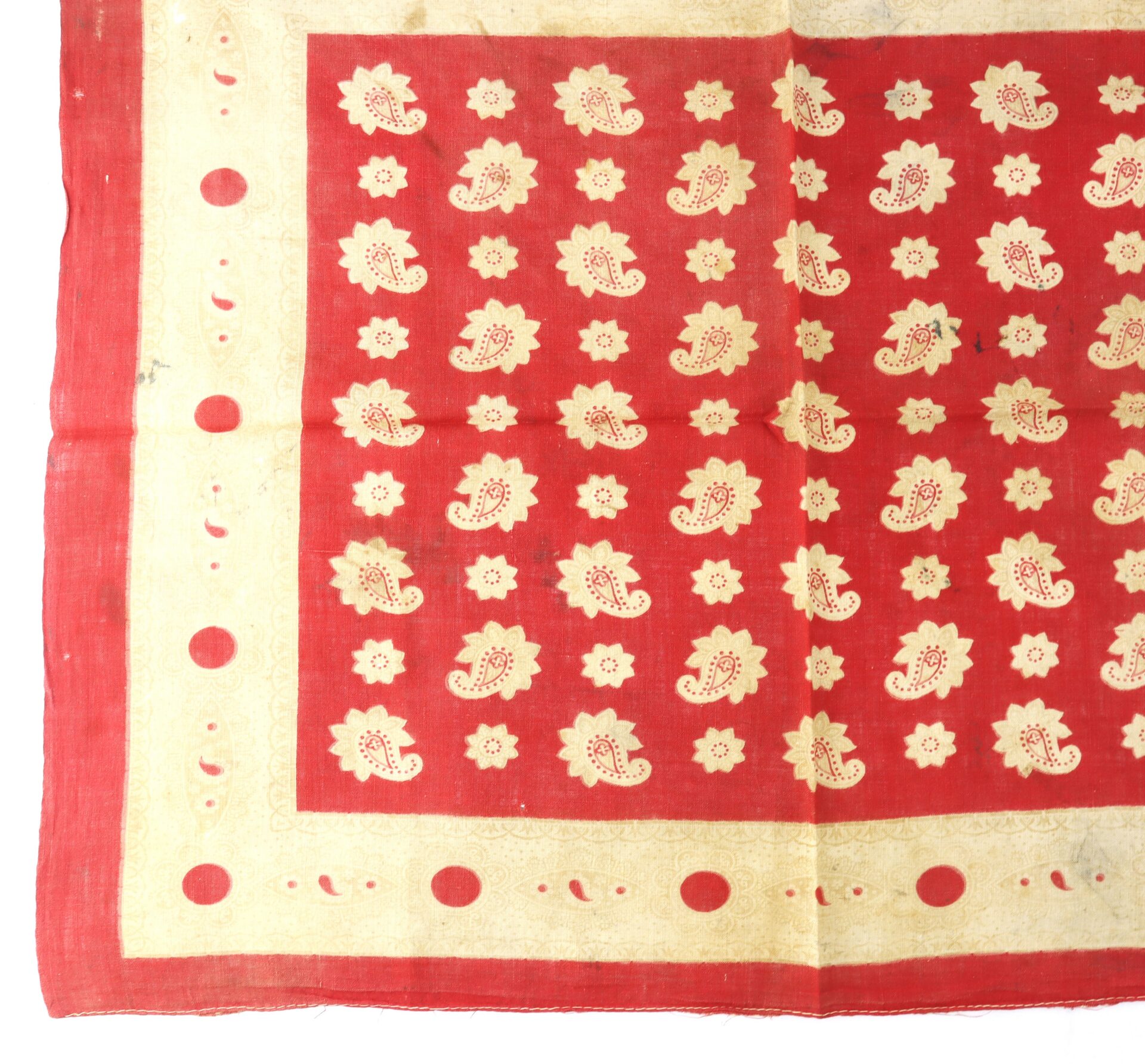Red fabric with a cream border, featuring a repeating pattern of cream paisleys and floral motifs in the center. The border has a row of large red dots spaced evenly.