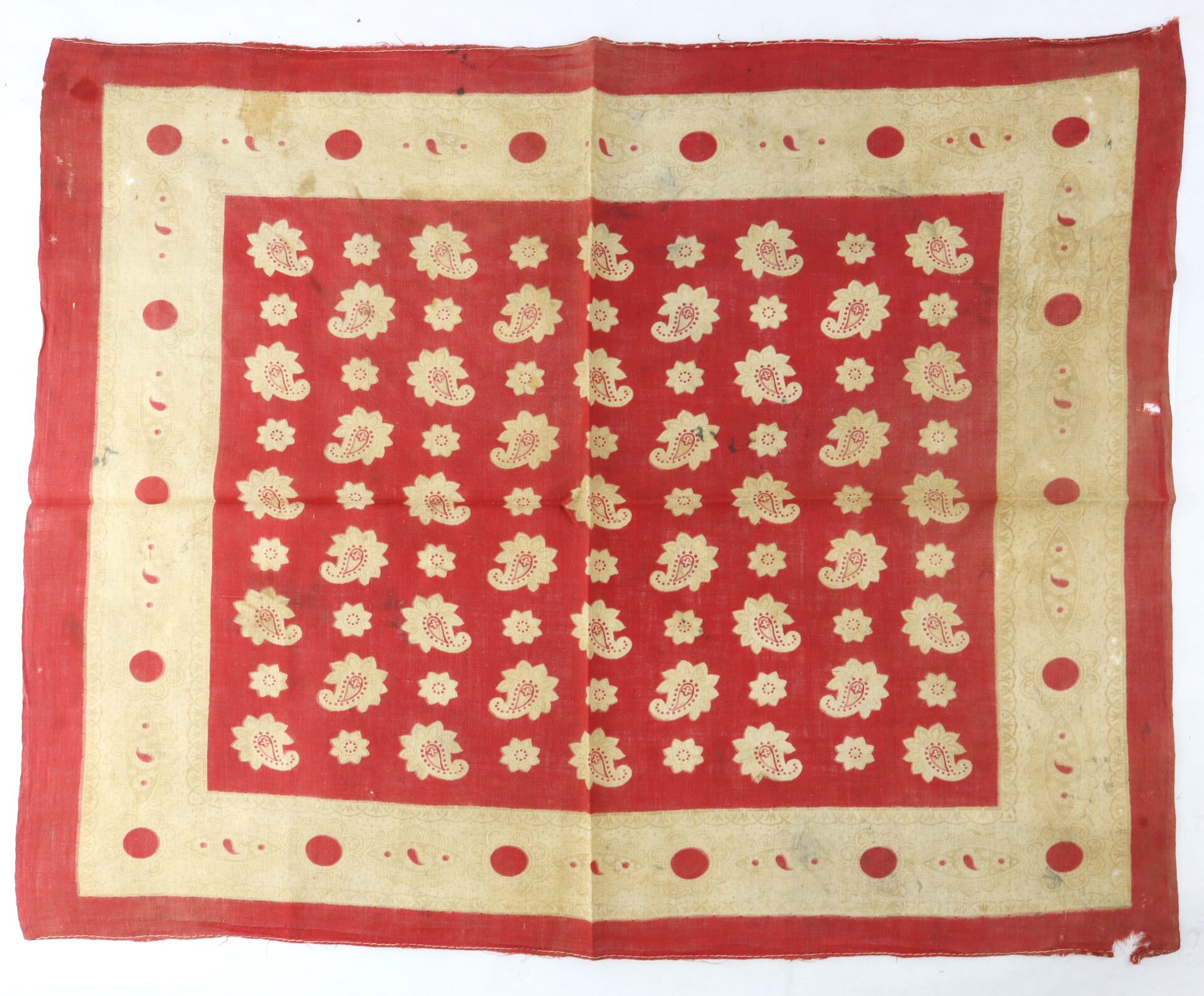 Red square textile with a gold floral pattern in the center and a gold border featuring polka dots and crescent shapes. The fabric appears slightly worn and is photographed on a white background.