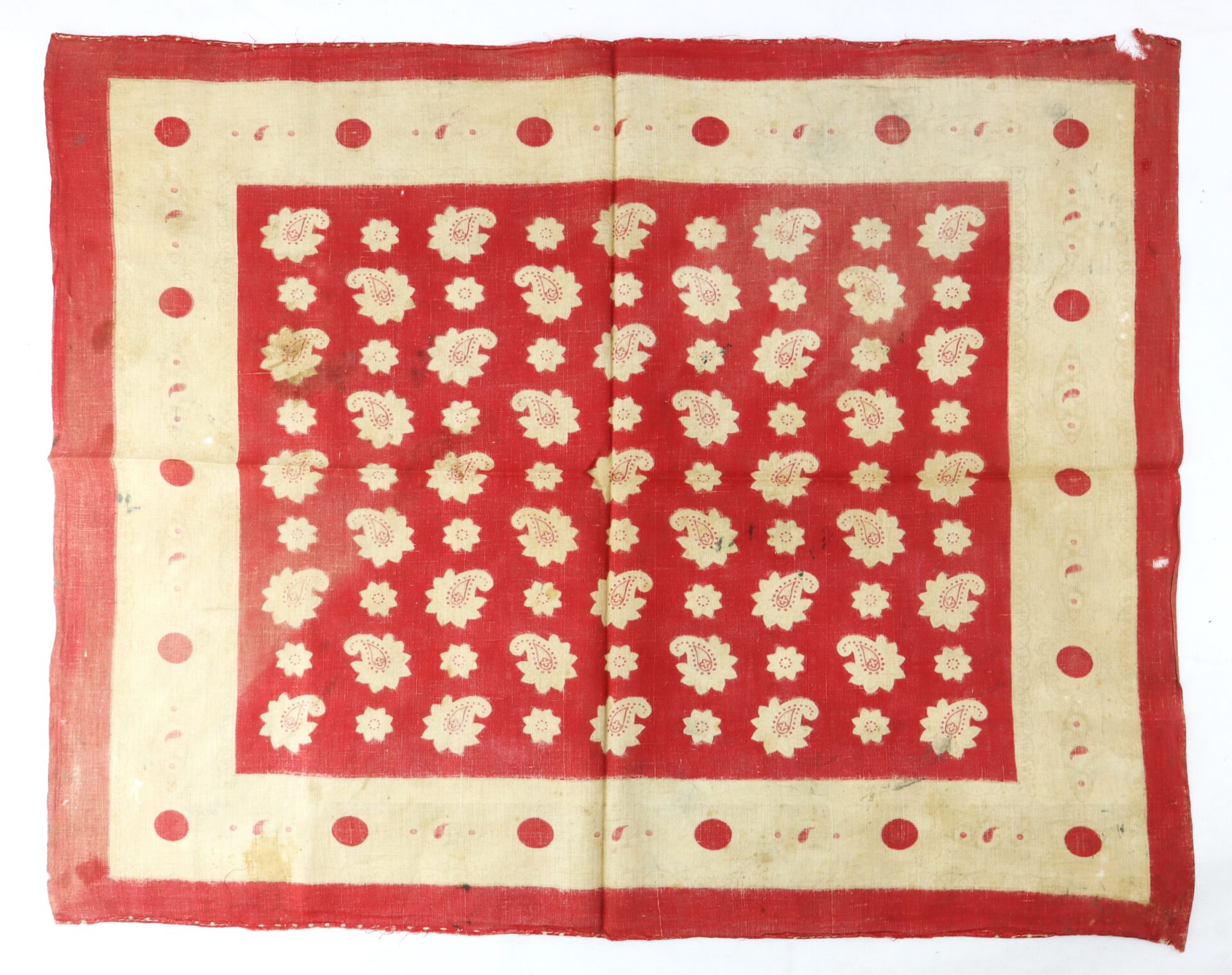 Red and beige square cloth with a border of red dots and a central pattern of beige floral motifs on a red background.