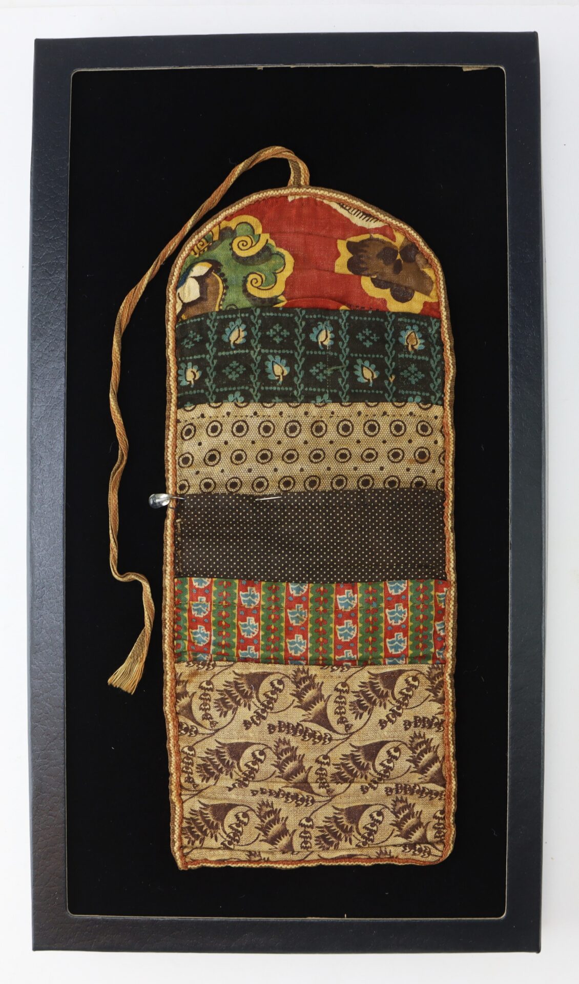 A rectangular patchwork fabric pouch with a flap and tie, featuring various patterned fabrics, displayed on a black background.