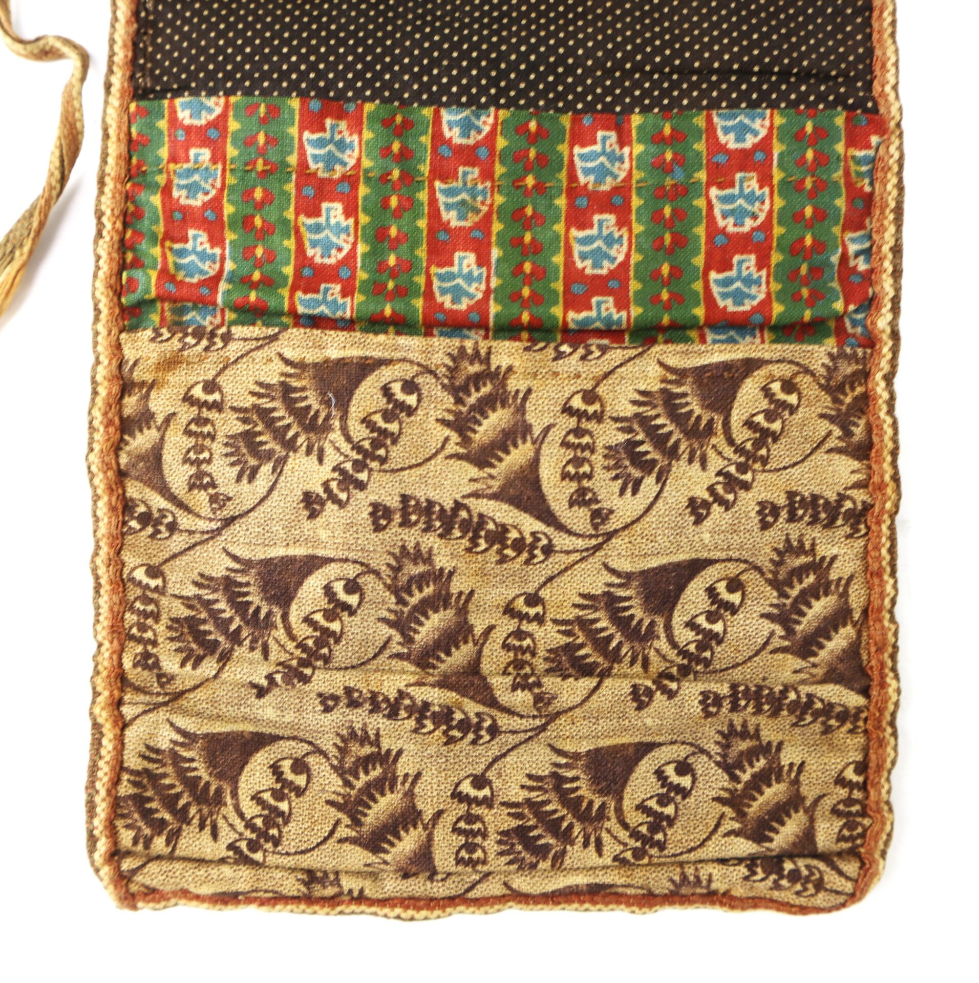 A close-up of a textile pouch with a brown fern pattern on the flap and a body featuring red, green, and blue geometric floral designs.