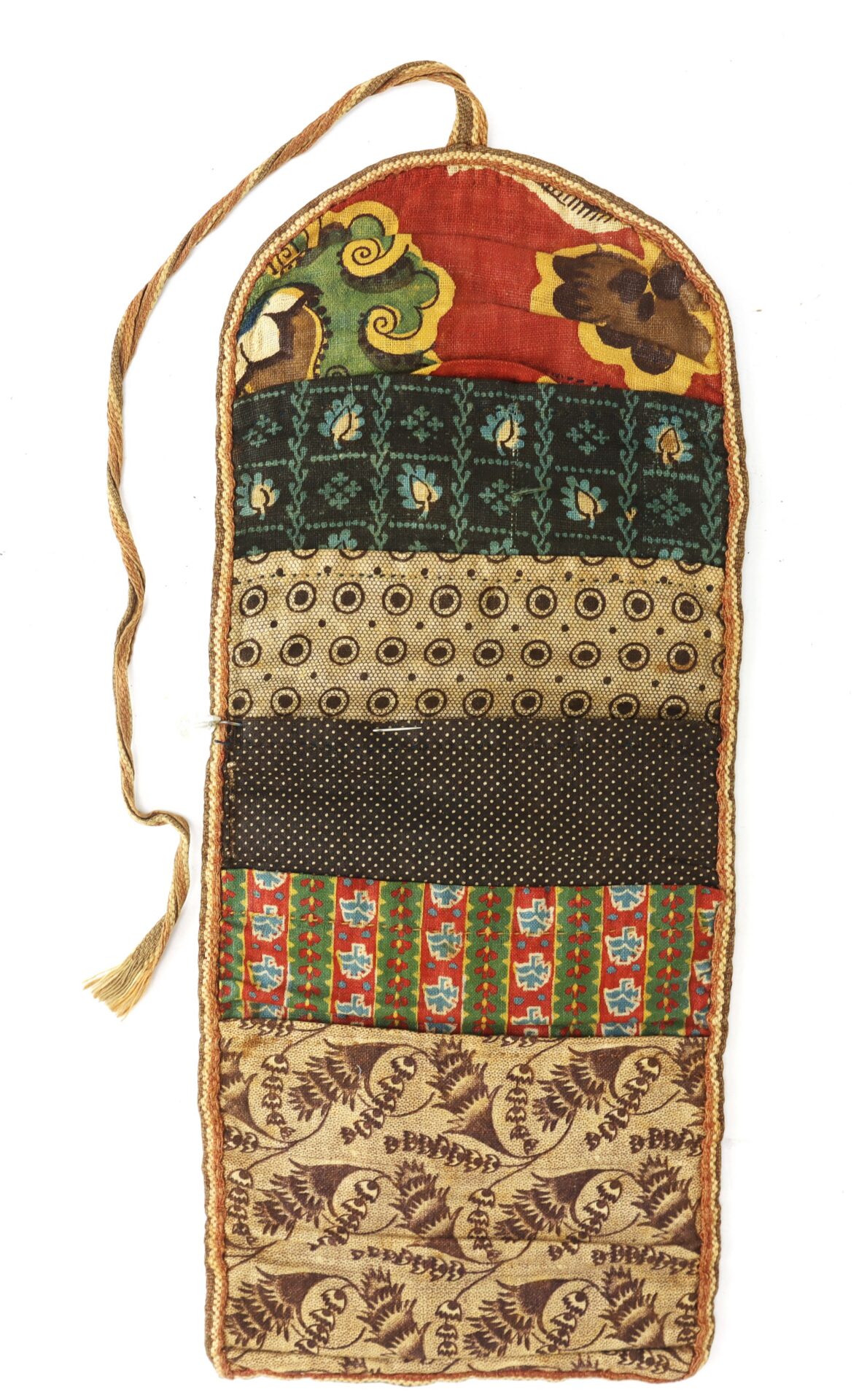A hanging textile organizer with six sections, each made from different patterned fabrics in red, green, brown, and tan, and a cord loop at the top for hanging.