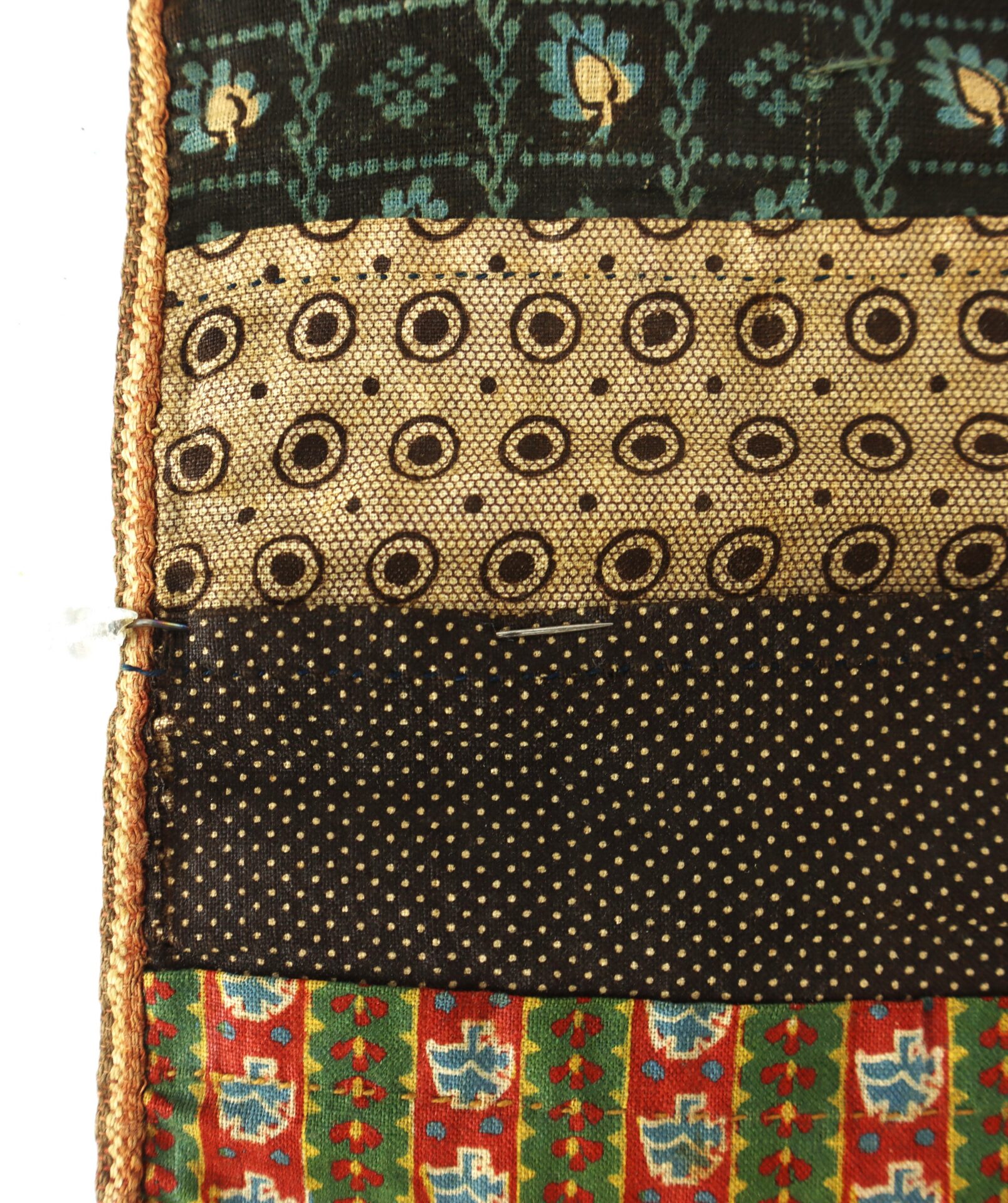 A close-up of a quilt with four patterned fabric strips and a safety pin attached near the left edge.