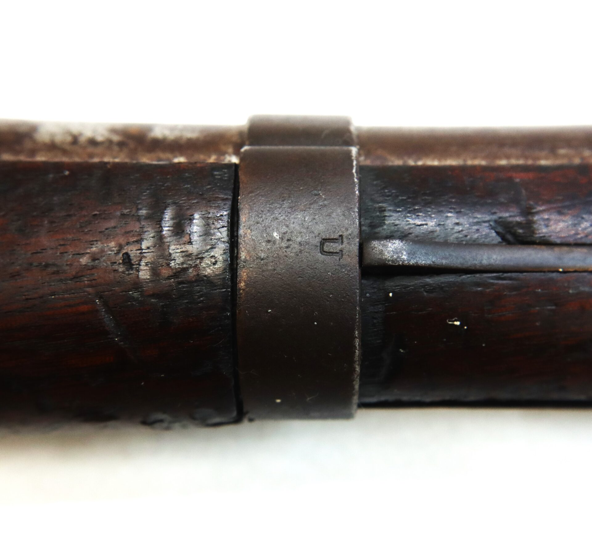 Close-up of a dark wooden object with a metal band around it, featuring a small stamped marking. The wood appears worn and scratched.