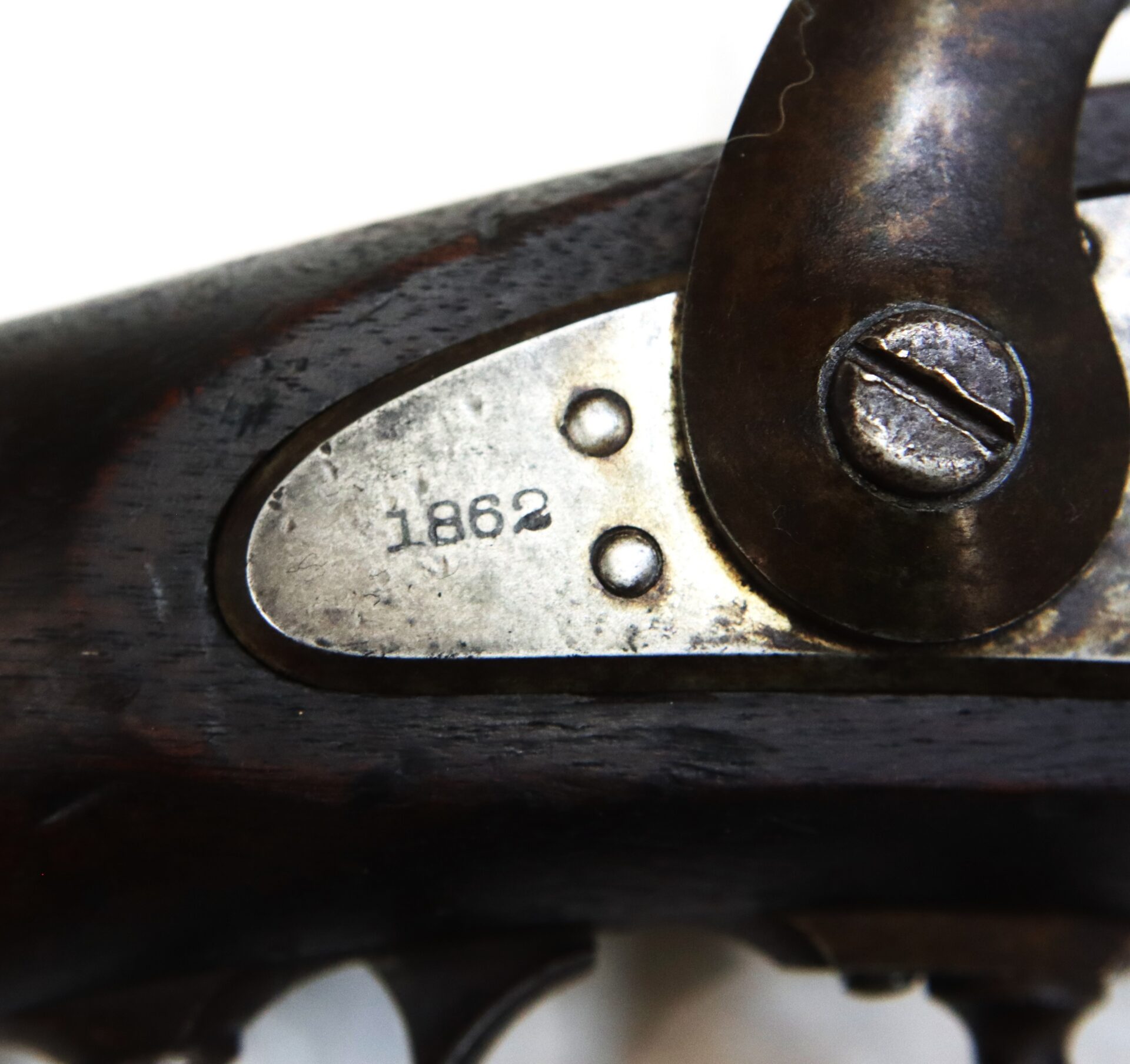 Close-up of an antique firearm’s metal plate, engraved with the year “1862,” showing part of a screw and dark wooden handle.