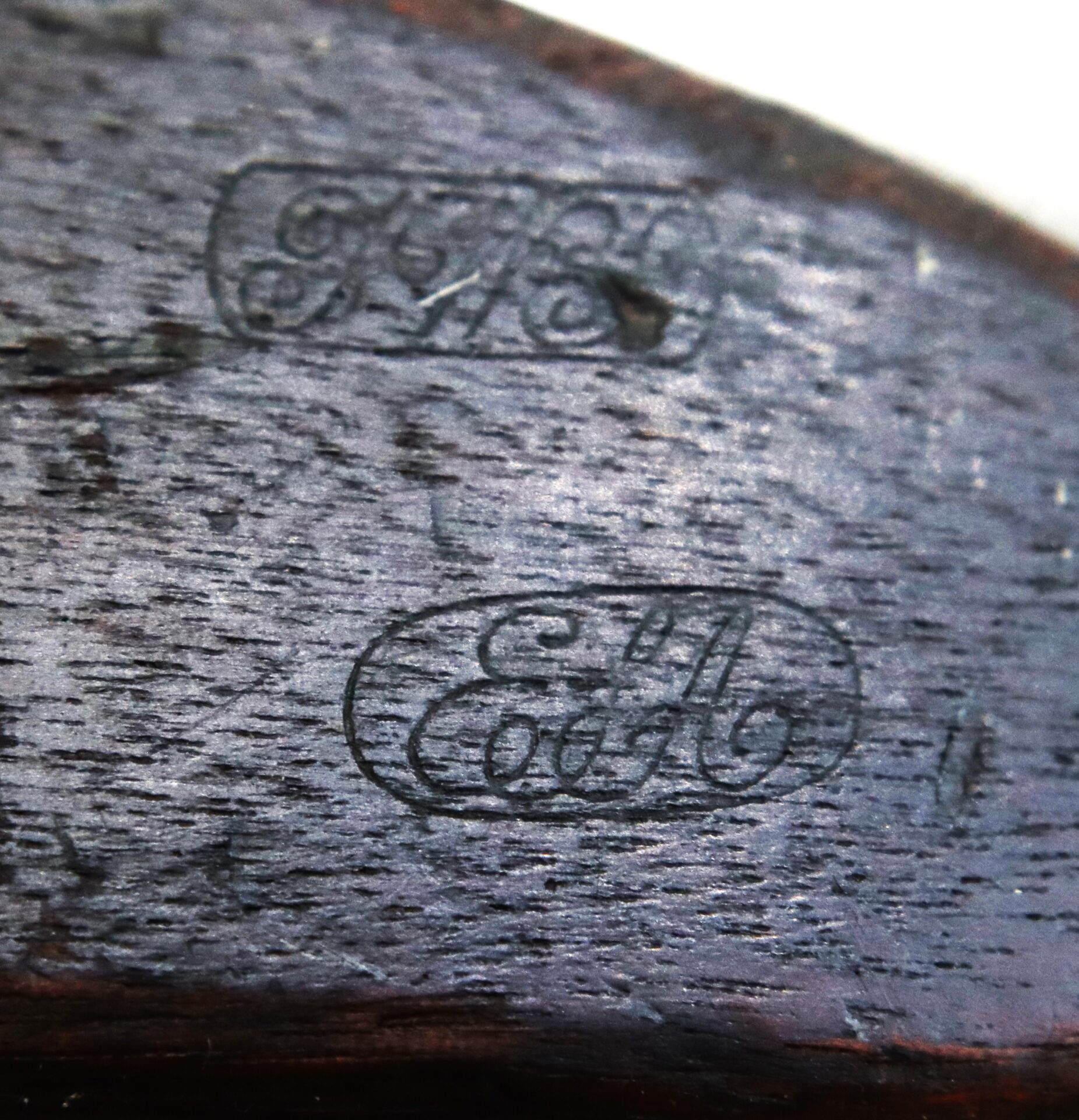 Close-up of two engraved stamps on weathered dark wood, one with ornate letters and the other reading “E. M. Coast” inside an oval.