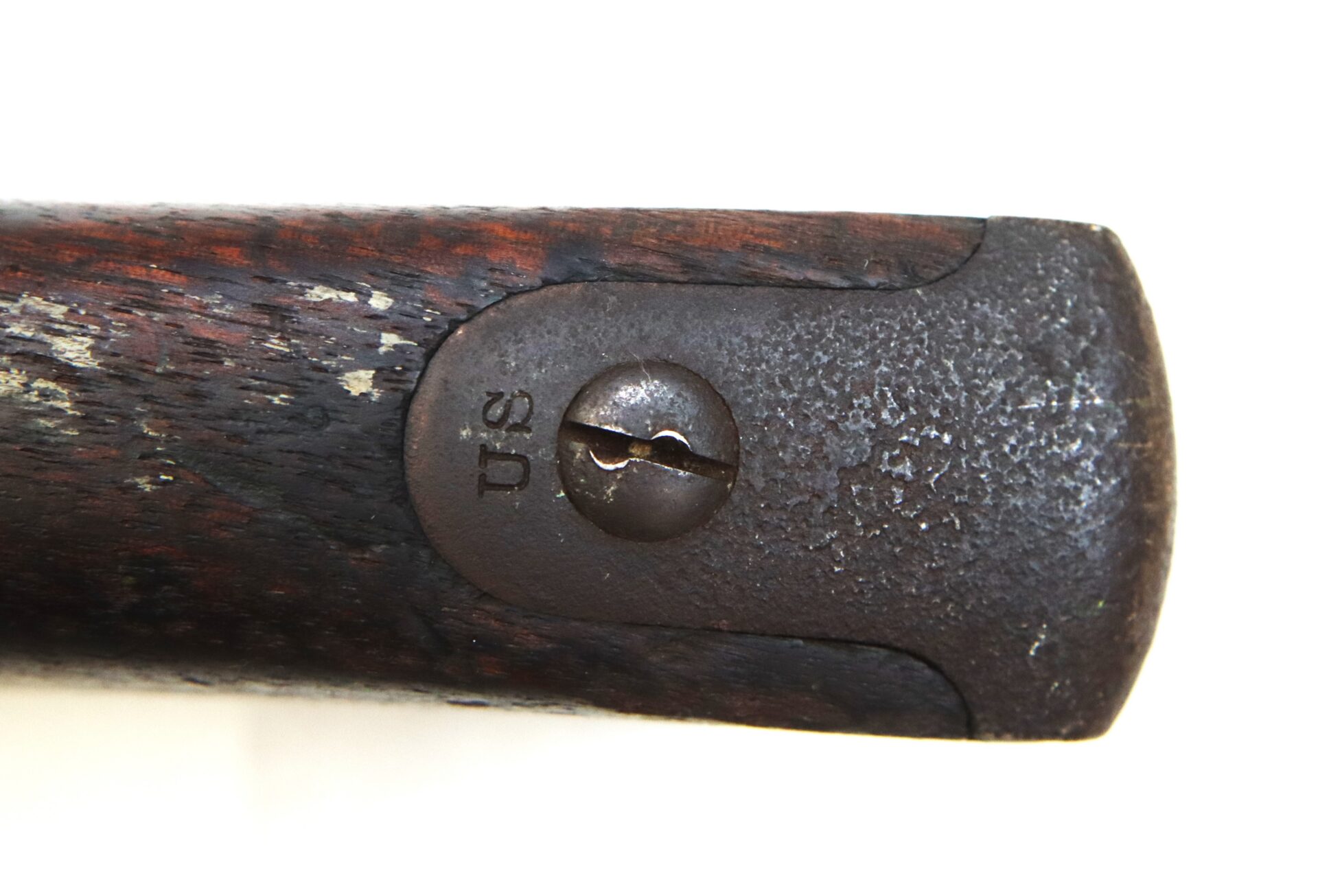 Close-up of a weathered wooden rifle buttplate with a metal end cap, showing a screw and the engraved letters “US.”.