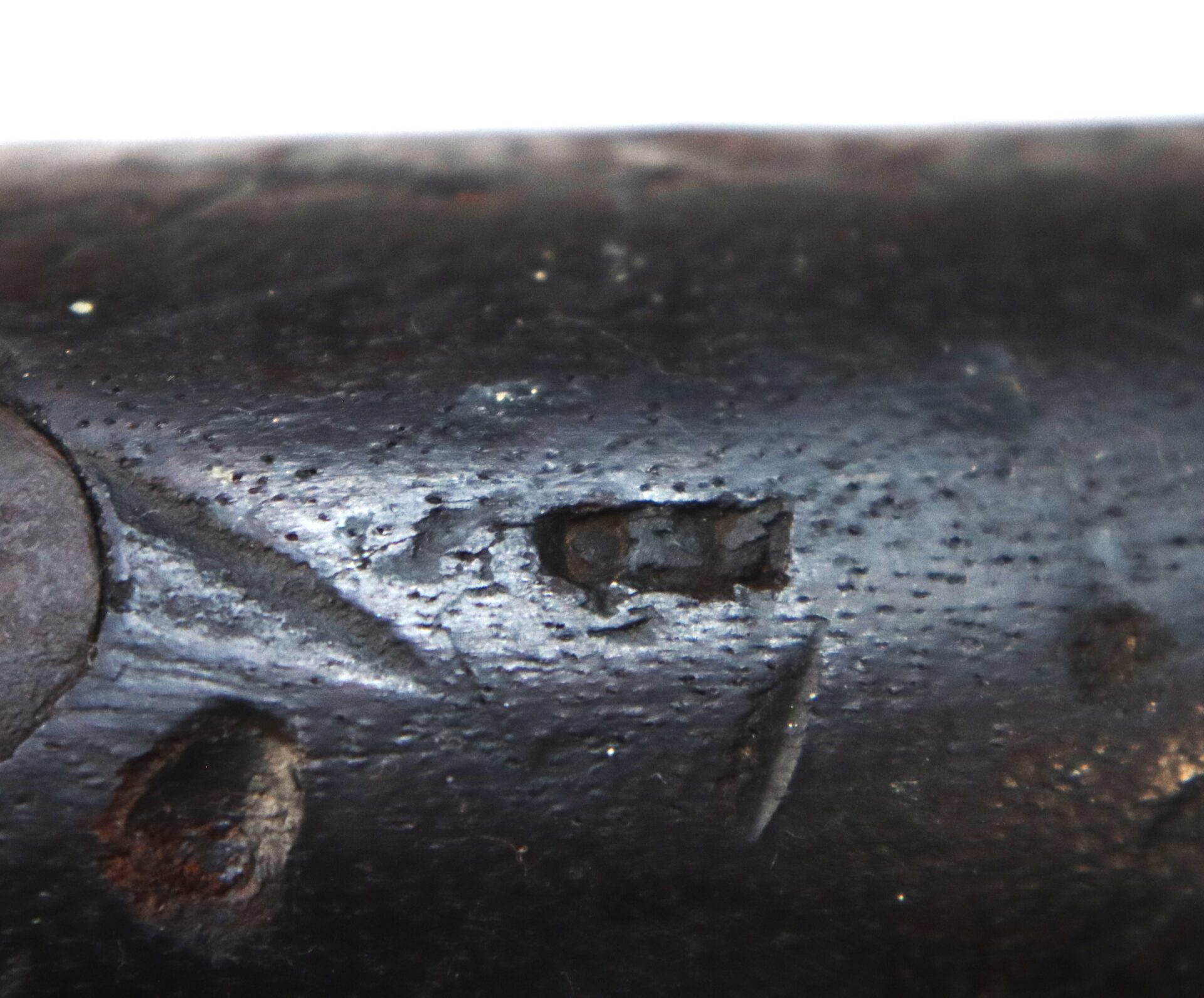 Close-up of a dark, roughly textured wooden surface with a small, rectangular carved indentation and other minor scratches and marks visible.