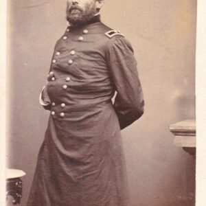 A bearded man in a double-breasted military uniform stands with one arm behind his back, facing the camera.