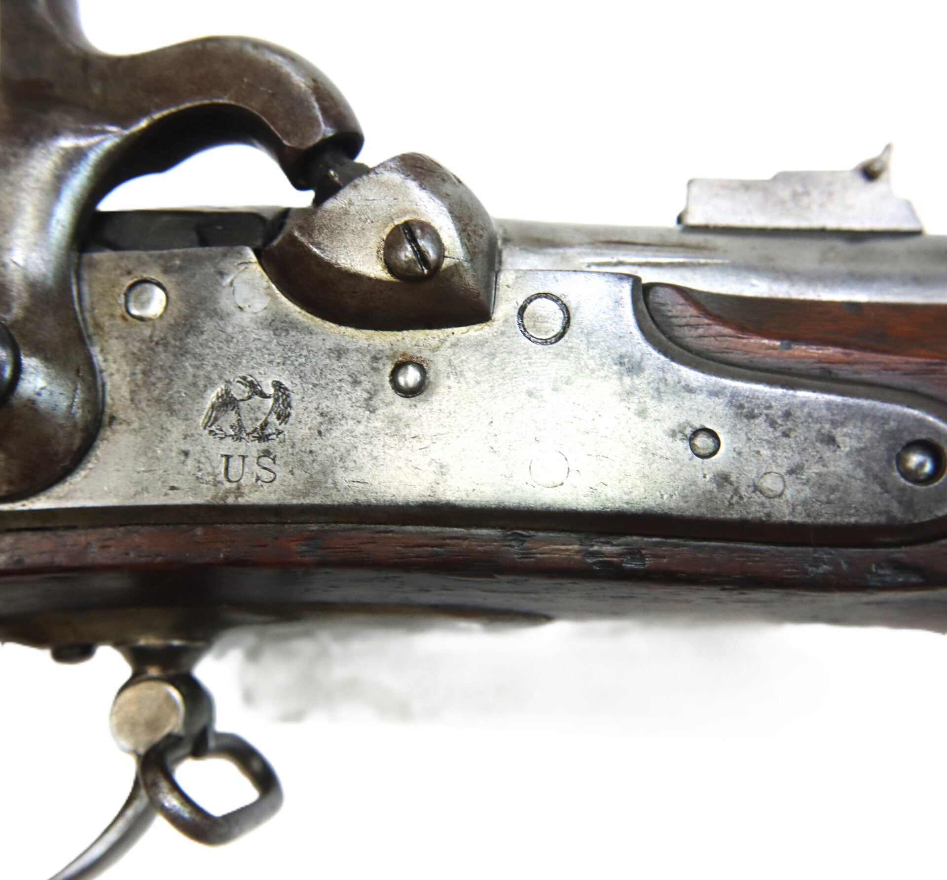 Close-up of a metal rifle receiver with a US eagle stamp and “US” marking, showing part of the hammer, trigger guard, and wooden stock.