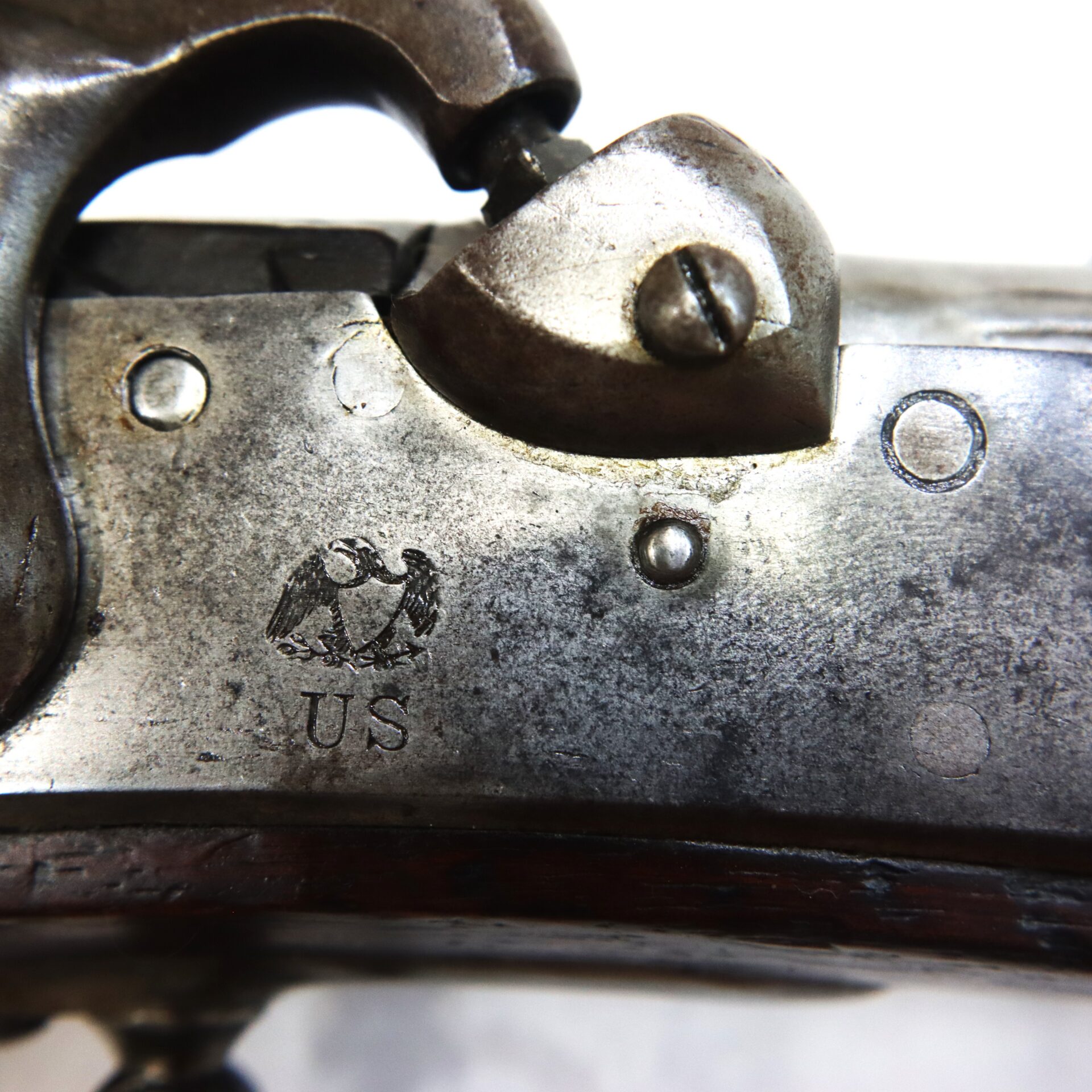 Close-up of a metal firearm part with an engraved eagle, the letters “US,” and visible screws on a worn surface.