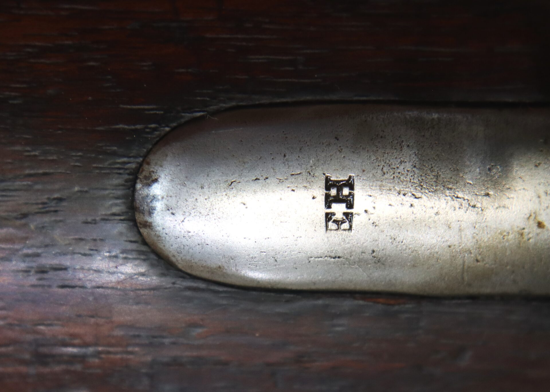 Close-up of a metal plate embedded in wood, featuring an engraved or stamped symbol consisting of two stacked horizontal sections.