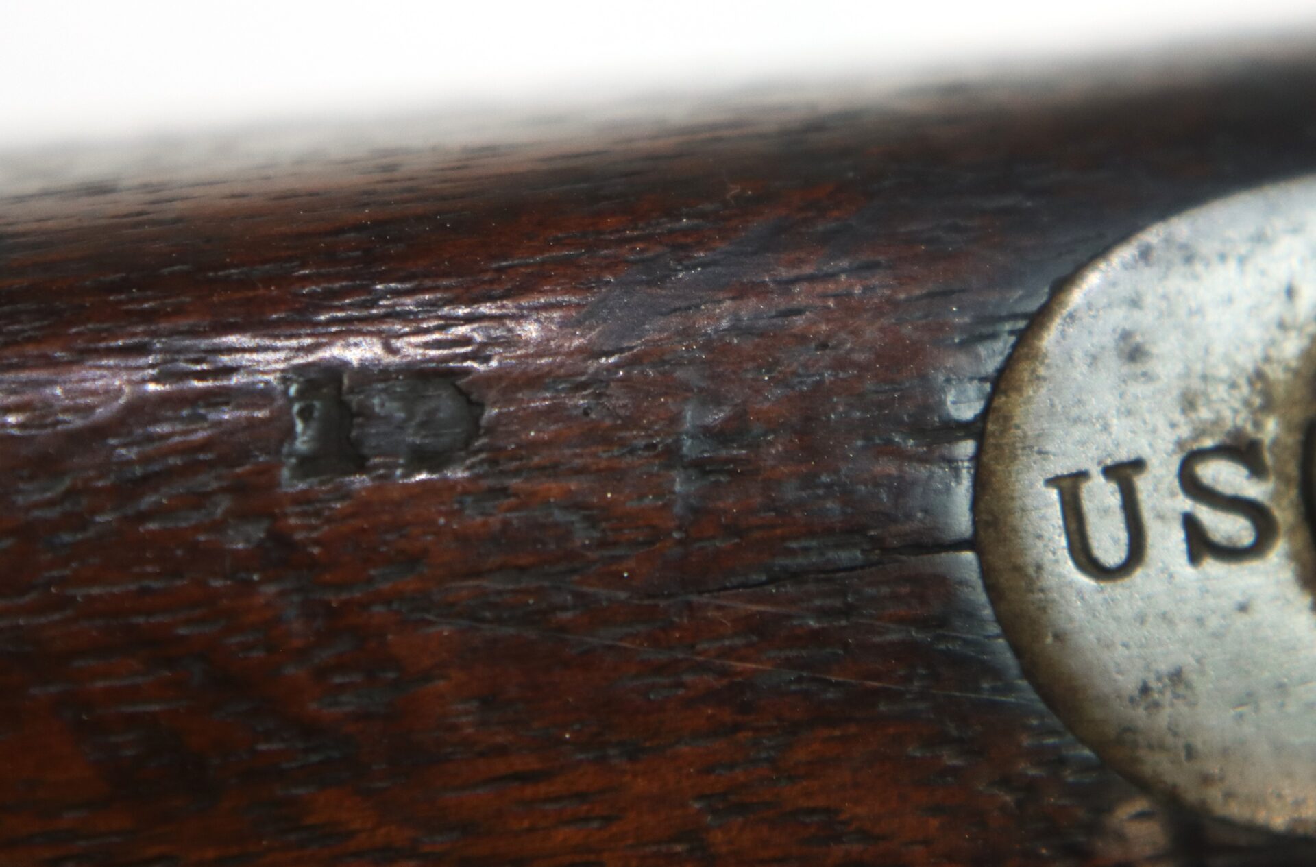 Close-up of a wooden object with a metal plate partially visible on the right side, displaying the letters “US” and some worn markings on the wood.
