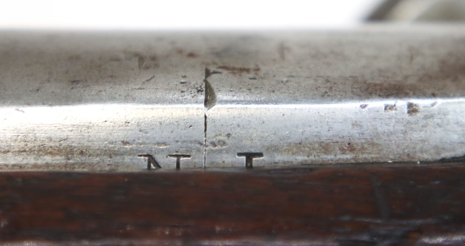 Close-up of a metal surface with a vertical crack and the letters “N T” stamped below it on a wooden base.