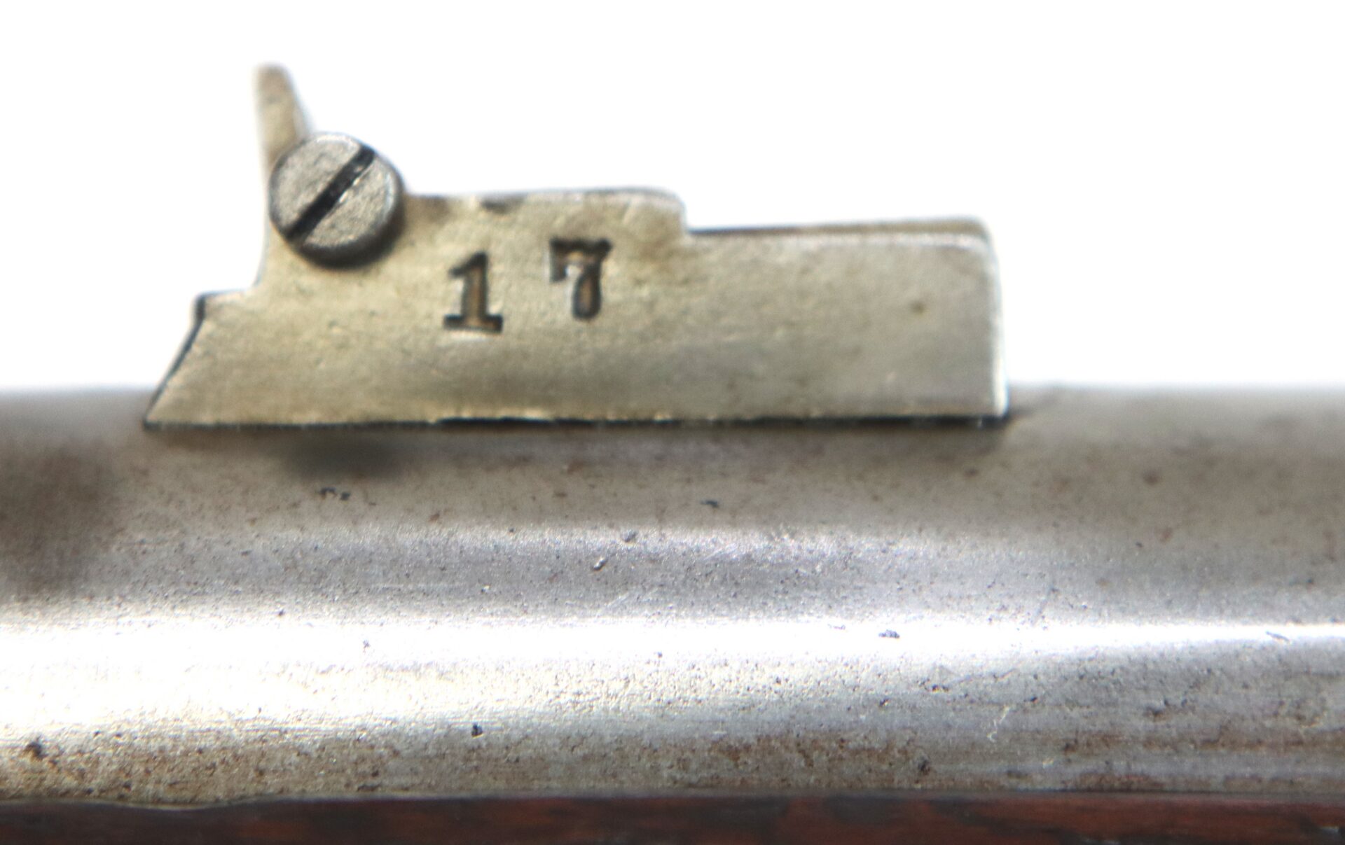 Close-up of a metallic gun sight with a screw and the number 17 engraved on it, attached to the top of a metal barrel.